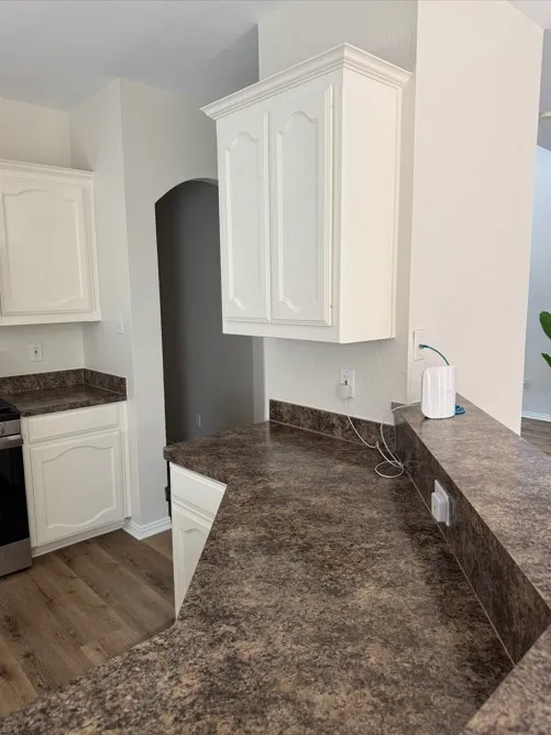 Full-height white cabinetry with crown molding, durable countertop surfaces, wood-finish flooring, and a stainless steel appliance