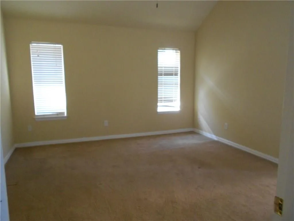 Vaulted ceiling, two windows with blinds, light-colored walls, and neutral carpeting