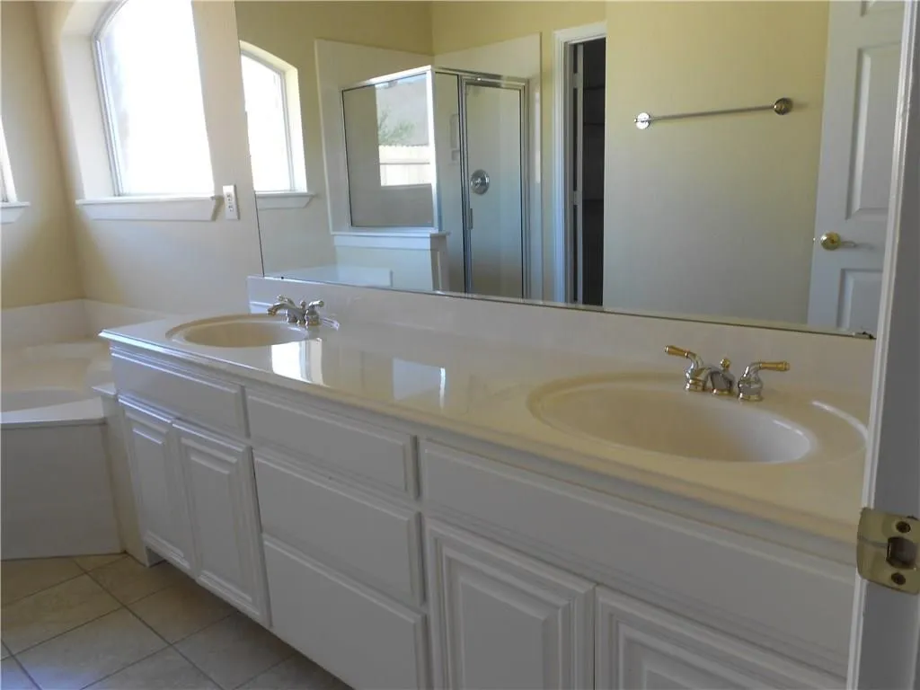 Double vanity with integrated sinks, white cabinetry, expansive wall mirror, and tiled flooring