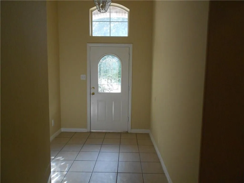 White entry door with decorative glass insert, arched transom window, overhead light fixture, and tile flooring