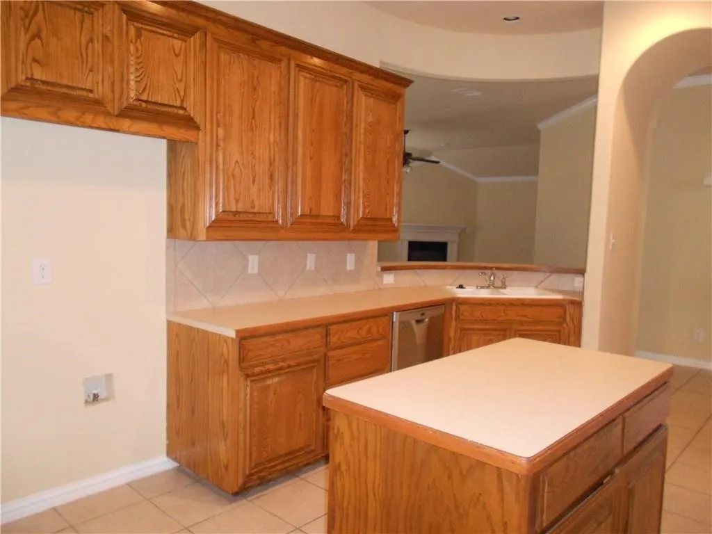 Wood-finish cabinetry with light countertops, diagonal tile backsplash, and a built-in stainless steel dishwasher