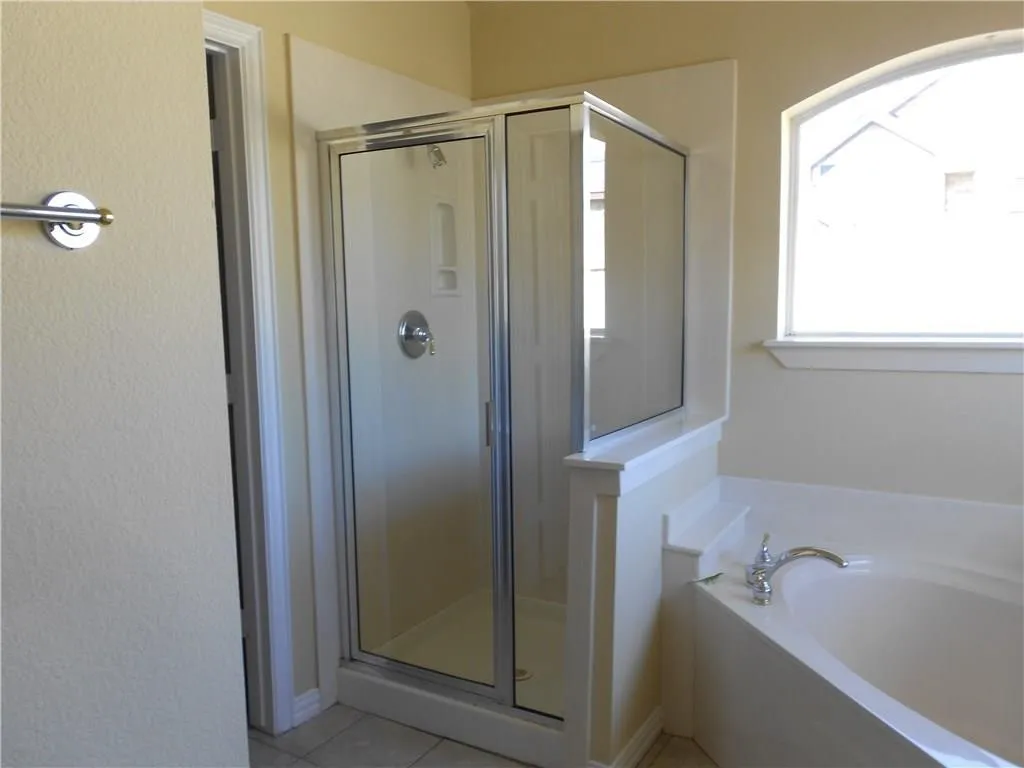 Glass-enclosed shower with chrome fixtures, an arched window, and a built-in corner bathtub