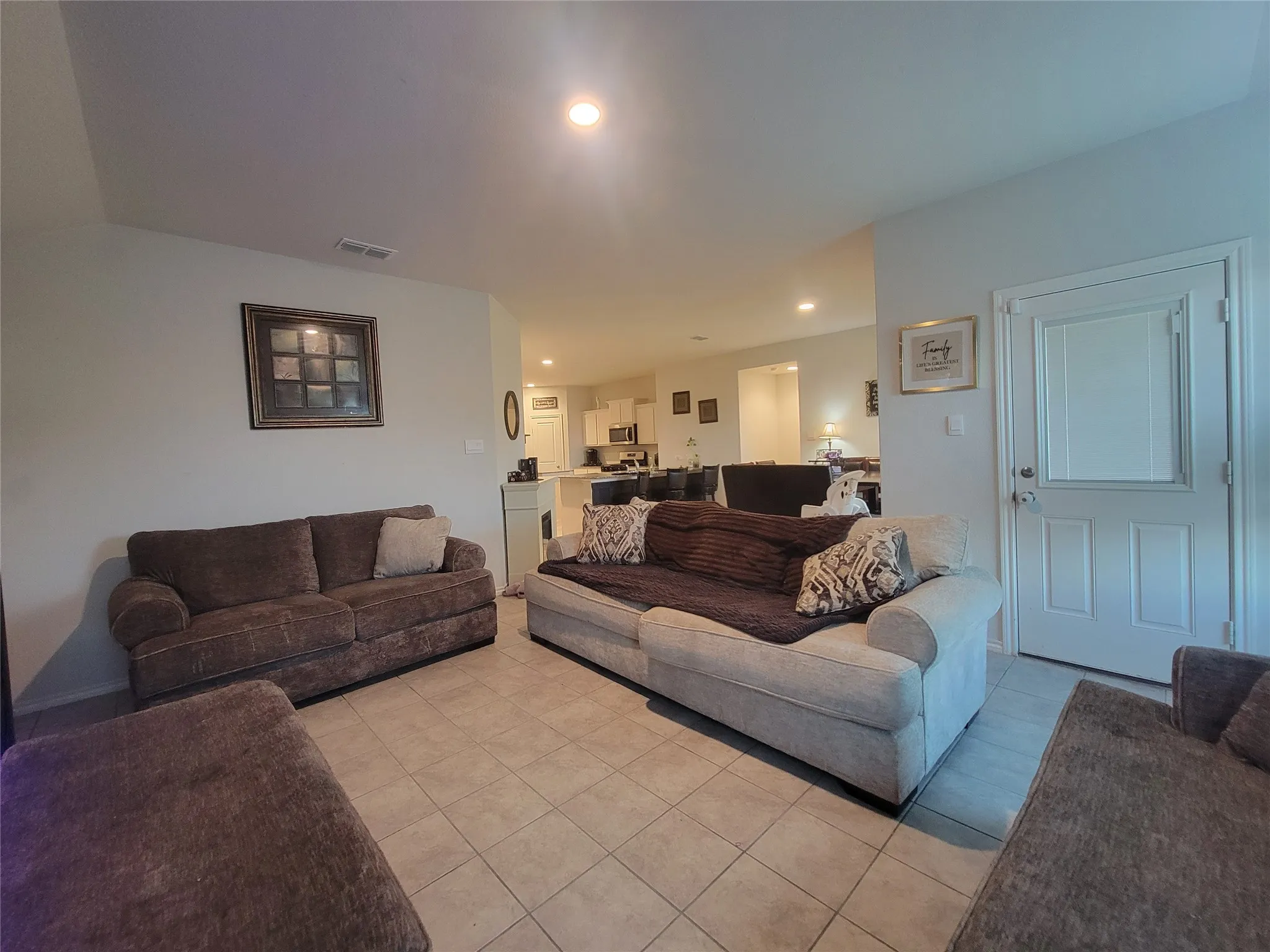 Recessed ceiling lighting, tiled flooring, paneled interior door, and a partially visible kitchen
