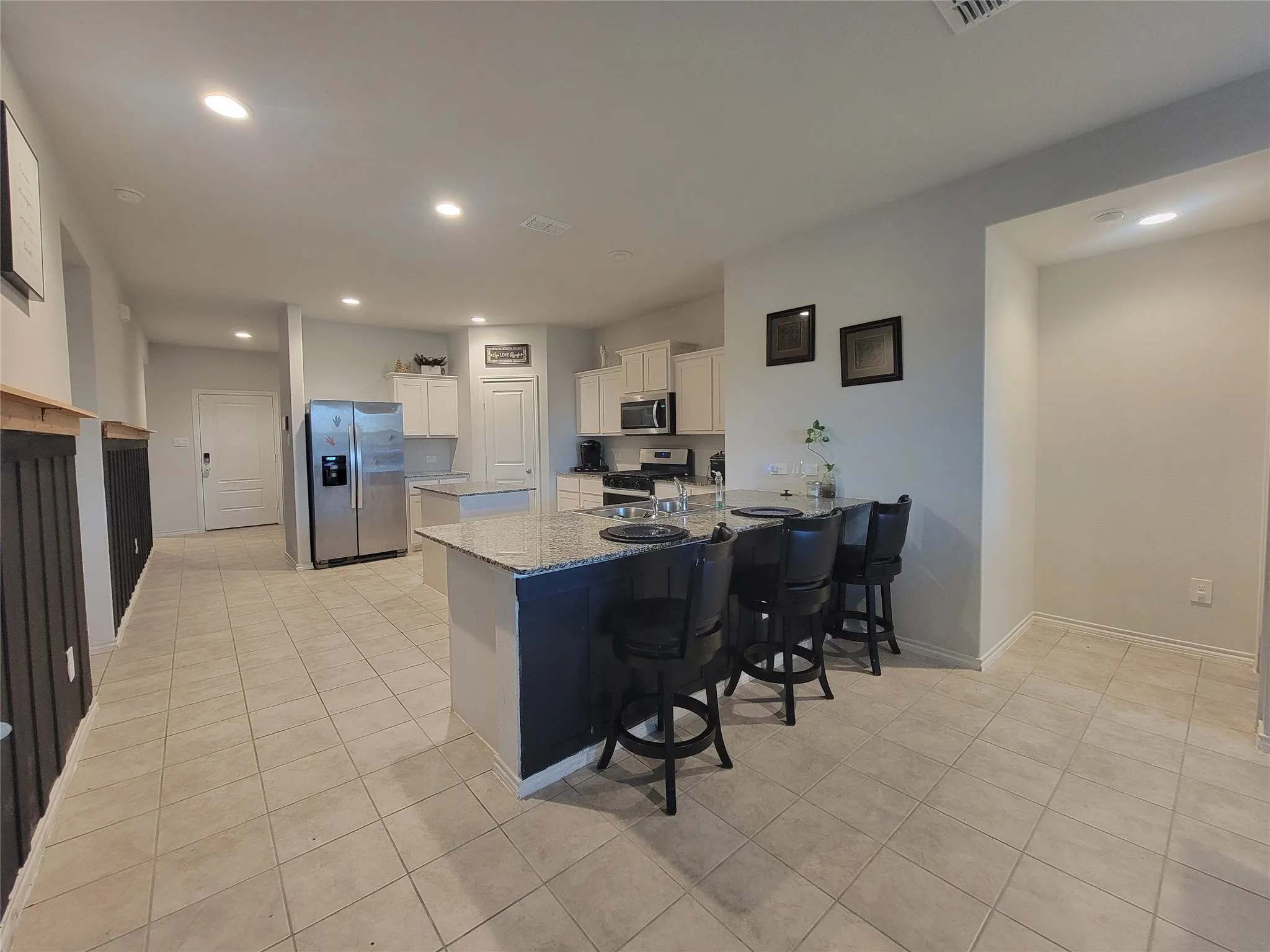 Open-concept kitchen with a large island featuring a granite-style countertop, white cabinetry, stainless steel appliances, and recessed lighting