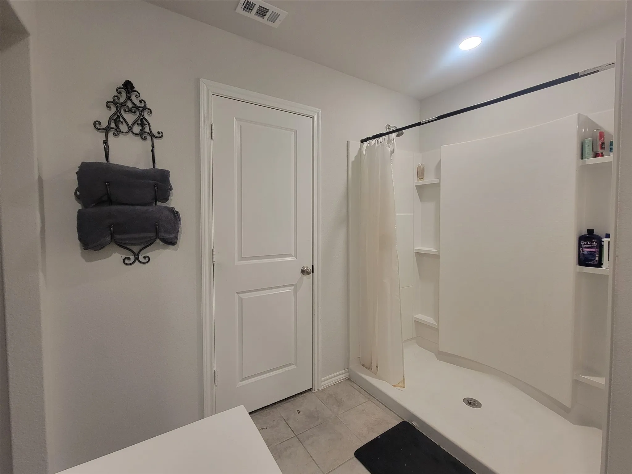 White shower enclosure with built-in shelving, overhead recessed lighting, and tile flooring