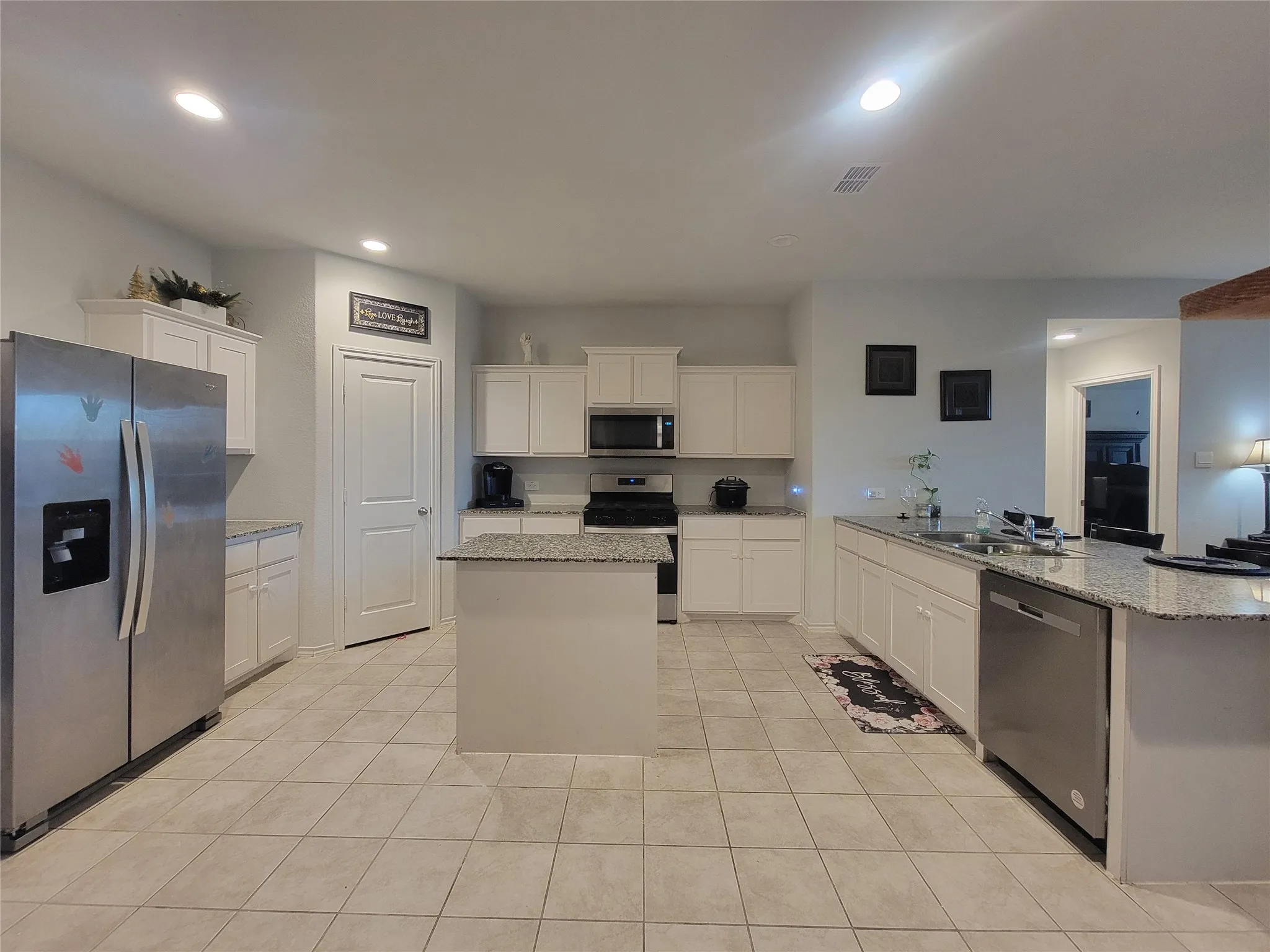 Kitchen featuring white cabinetry, light-toned tile flooring, granite countertops, stainless steel appliances, and a central island