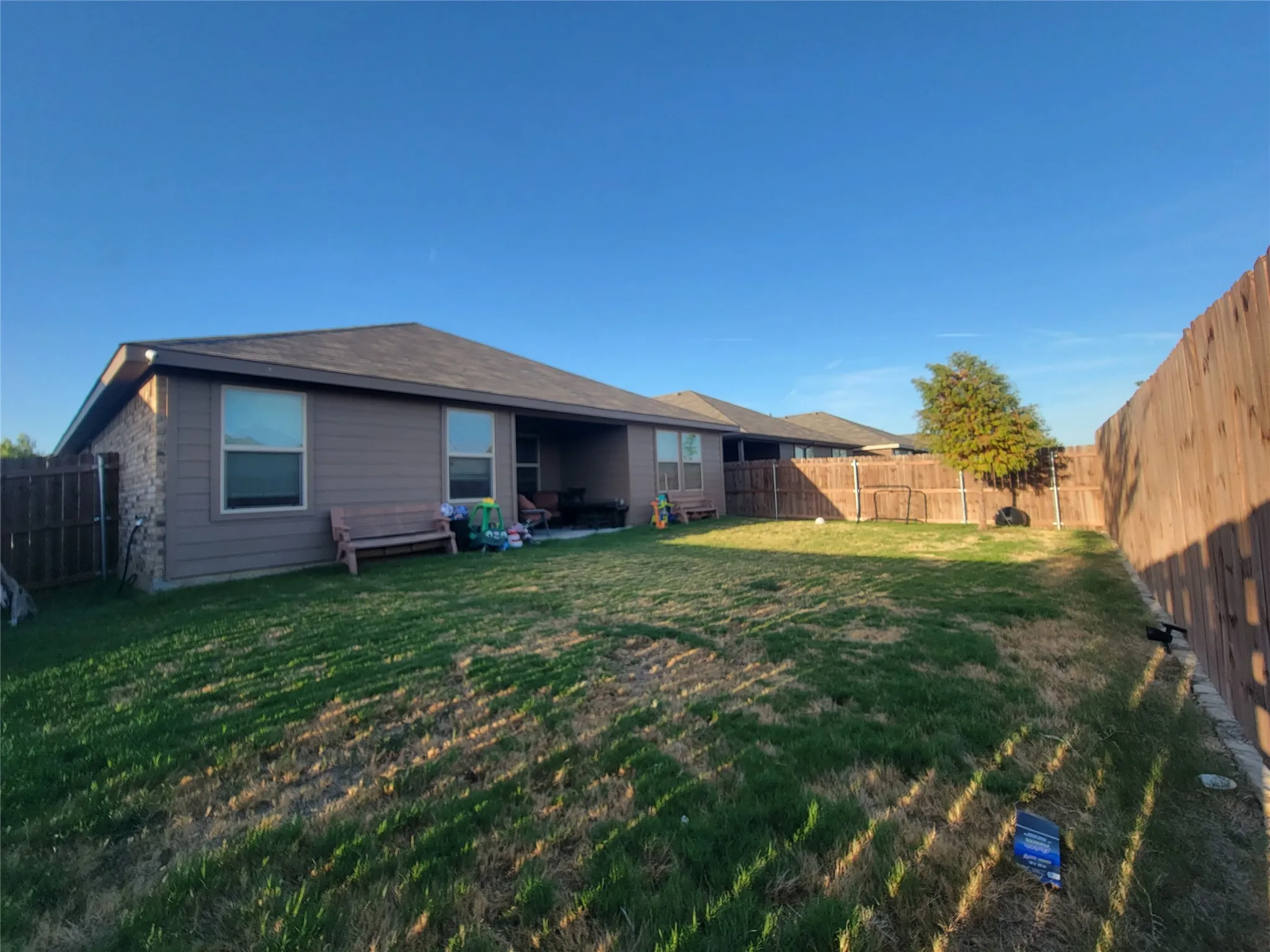 Expansive backyard with a manicured lawn, full privacy fencing, and a covered patio area