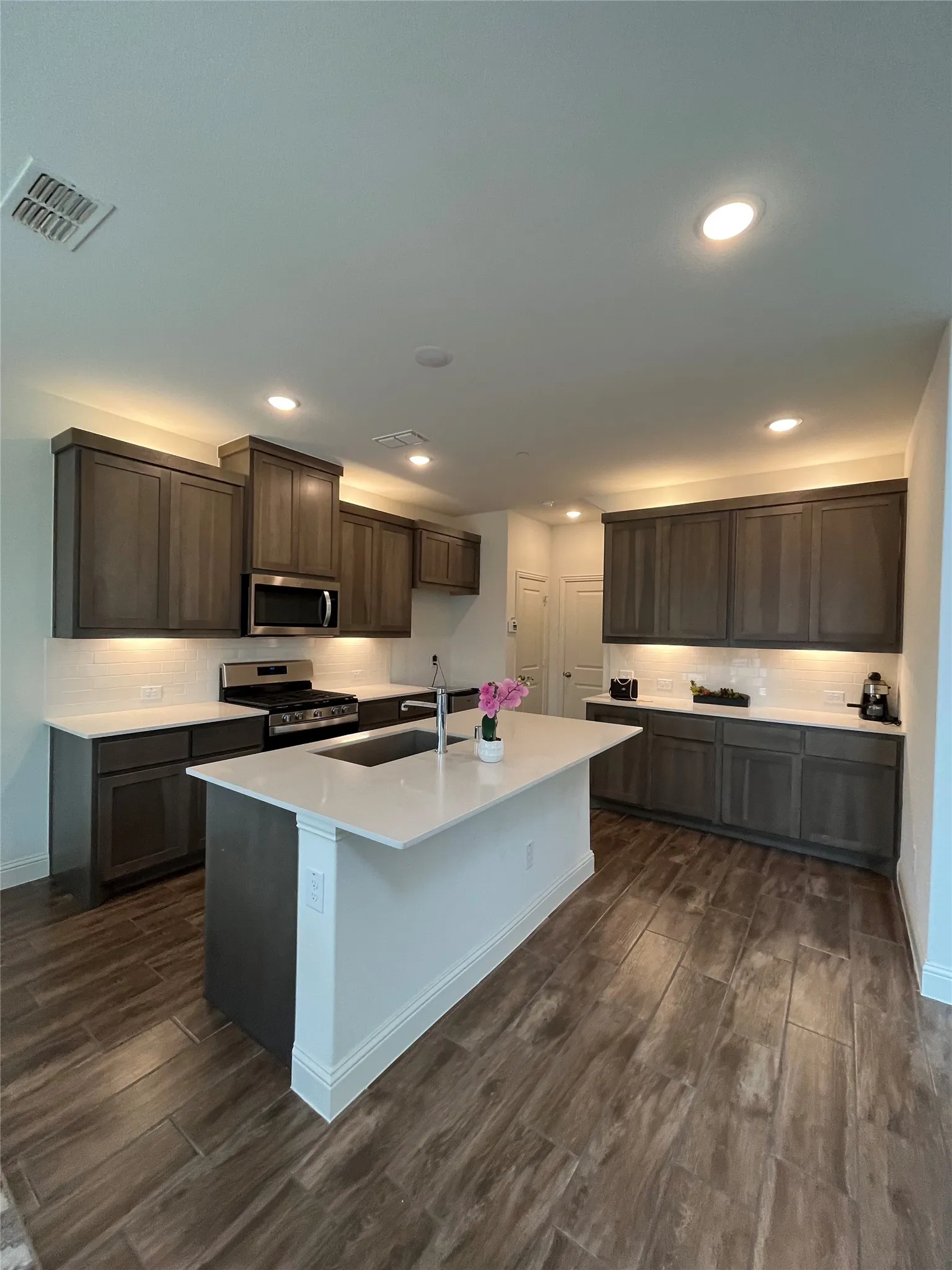 Kitchen featuring quartz, stainless steel appliances, rich wood cabinets, hardwood style floors, and an island with sink plus breakfast bar.  Extra cabinets and space for a coffee bar!