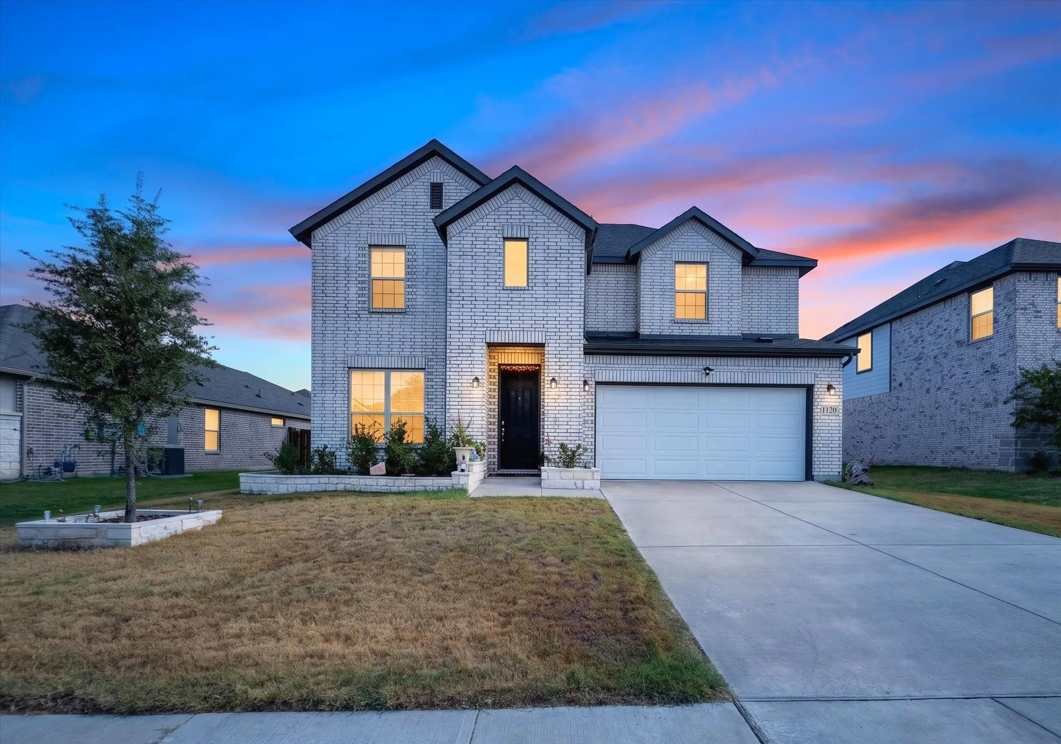 Two-story brick exterior, attached two-car garage, concrete driveway, and front landscaping