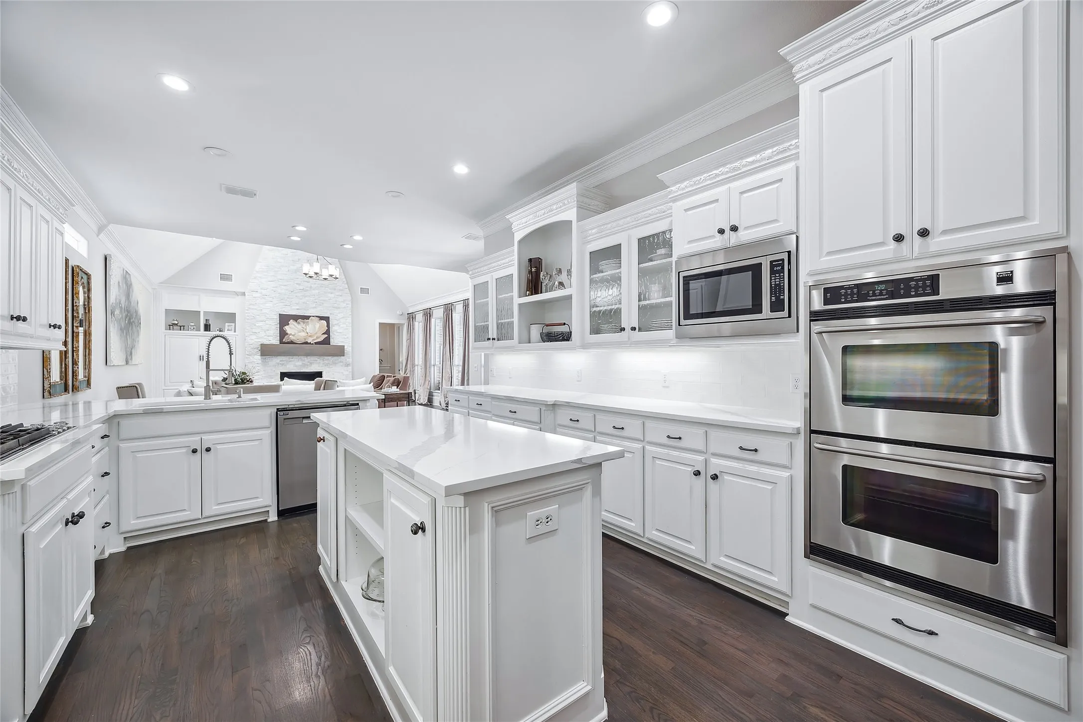 White cabinetry with black hardware, wood-finish flooring, white countertops, built-in double oven, and a built-in microwave