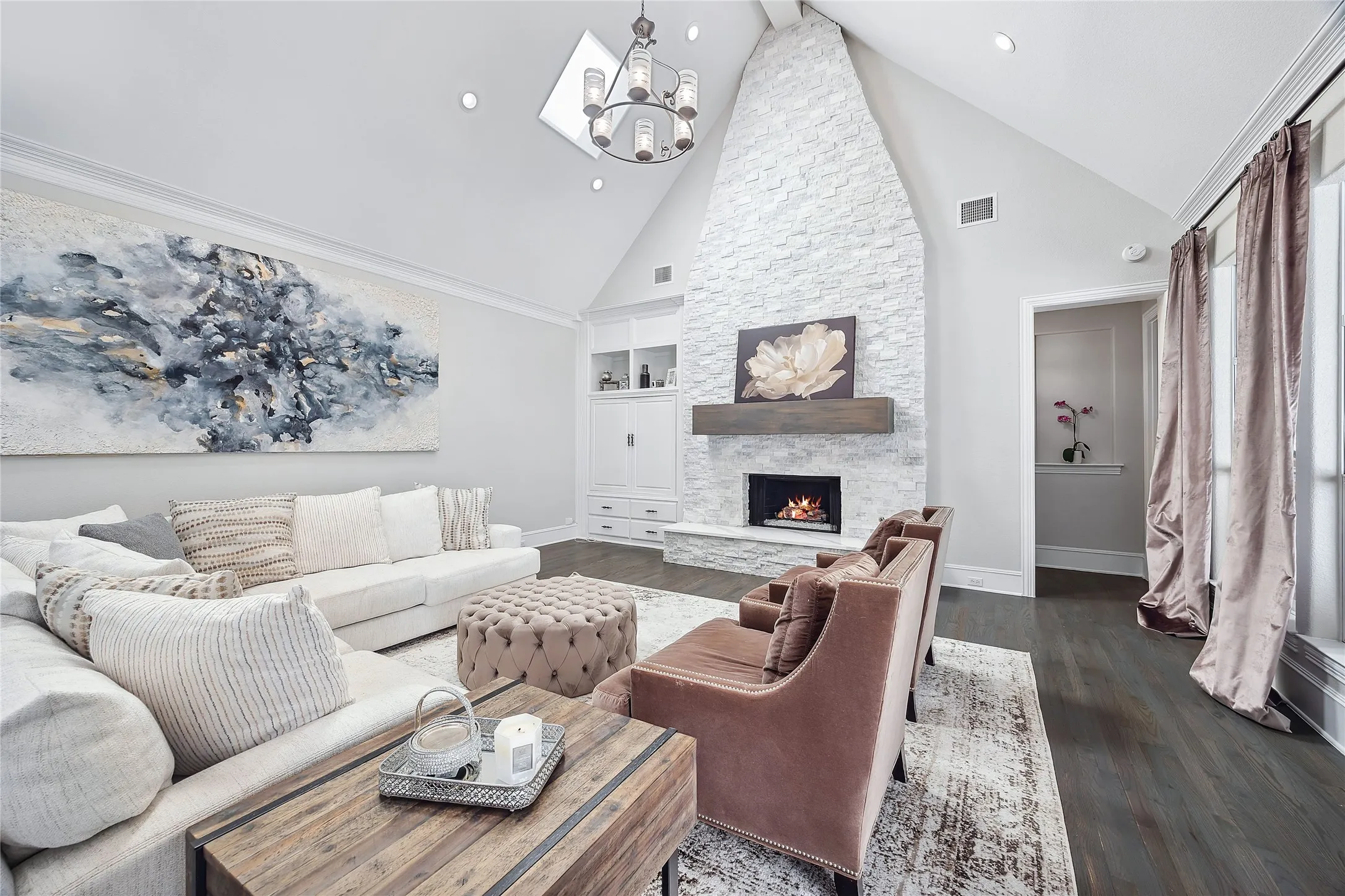 Vaulted ceiling with recessed lighting and skylight, stone-clad fireplace with wood mantle, built-in cabinetry, and dark wood-finish flooring