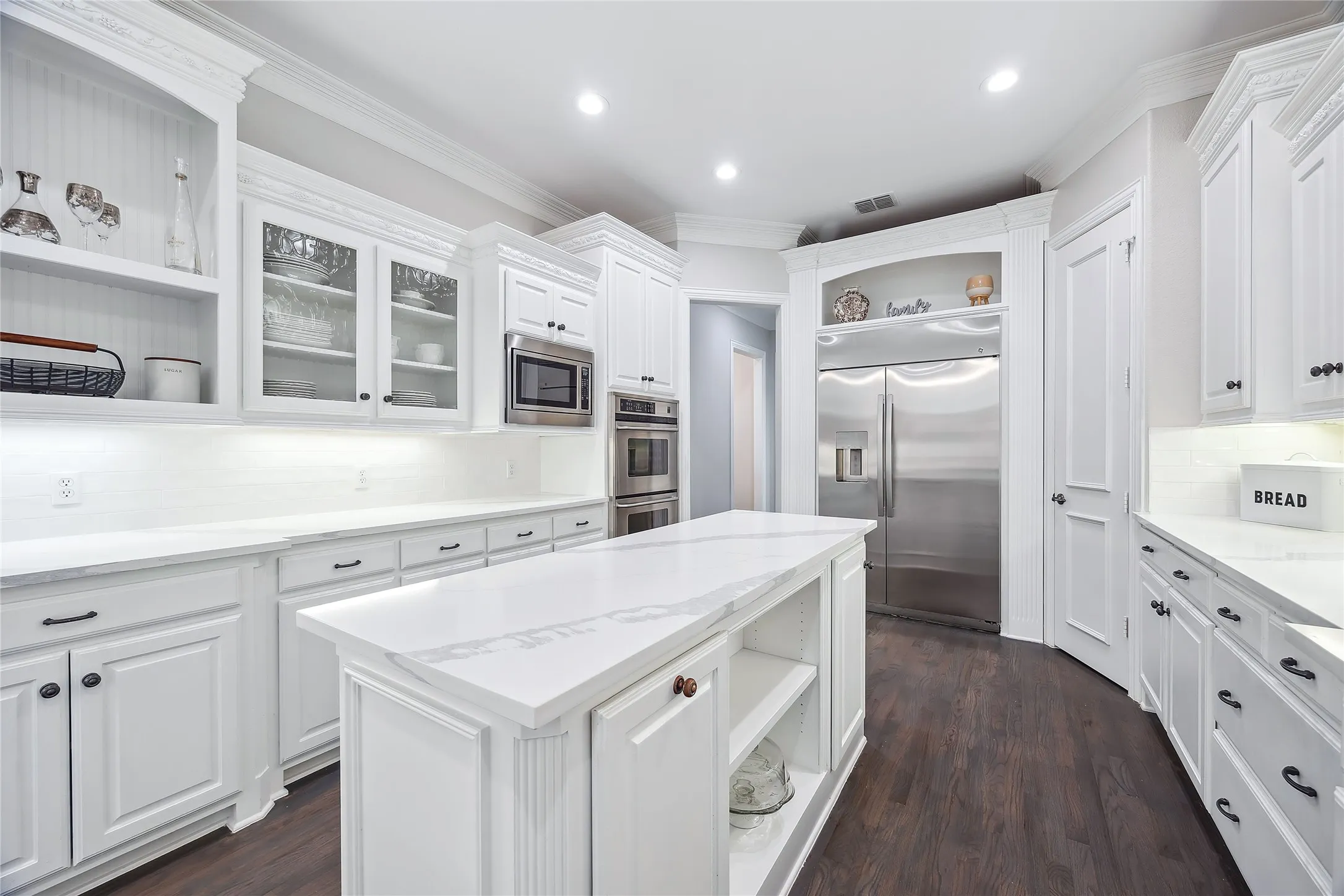 Spacious kitchen featuring an expansive central island with a stone countertop, white cabinetry with dark hardware, stainless steel appliances, and wood-finish flooring