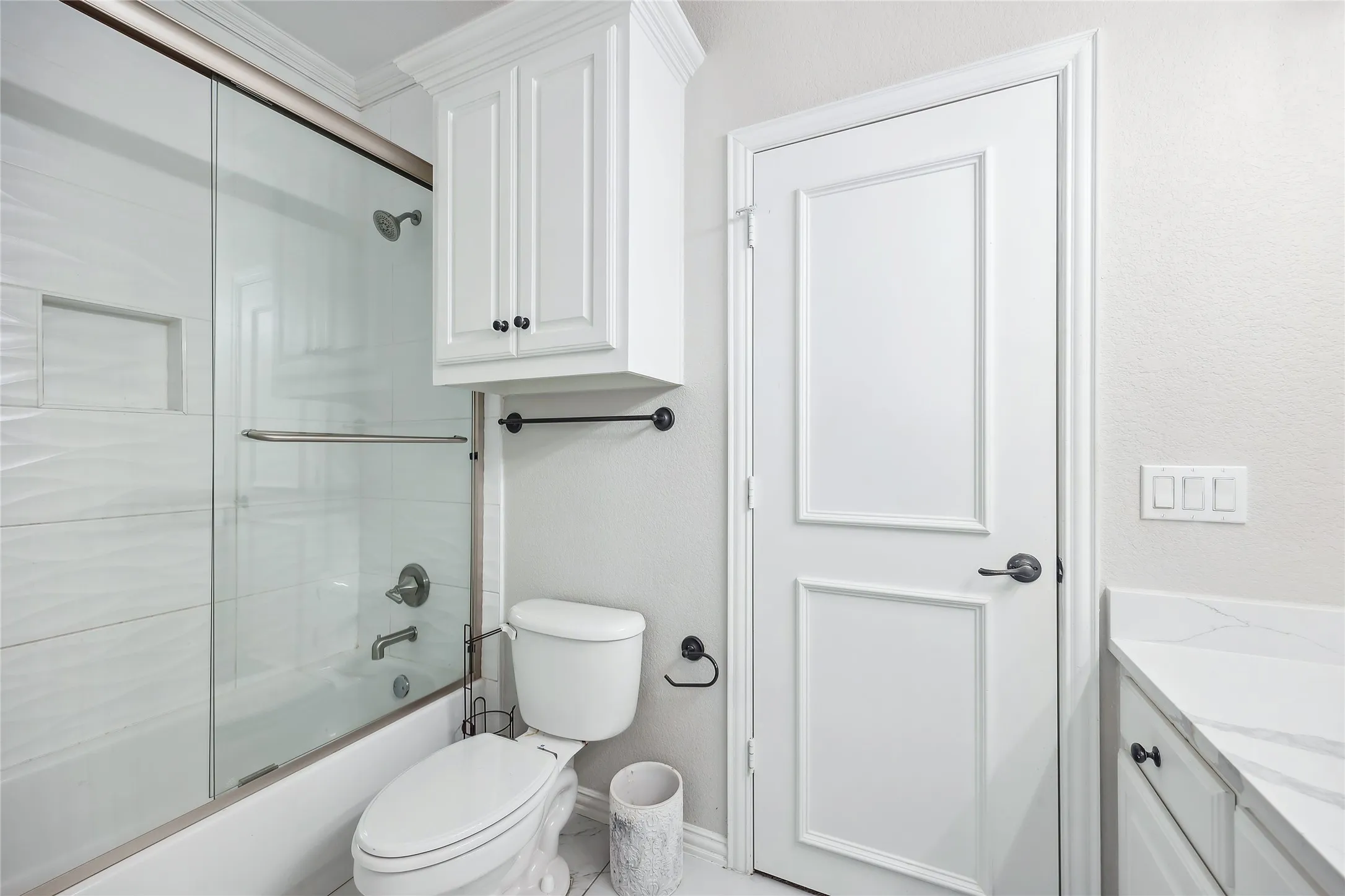 Bathtub with sliding glass shower door, recessed shower niche, and brushed nickel fixtures