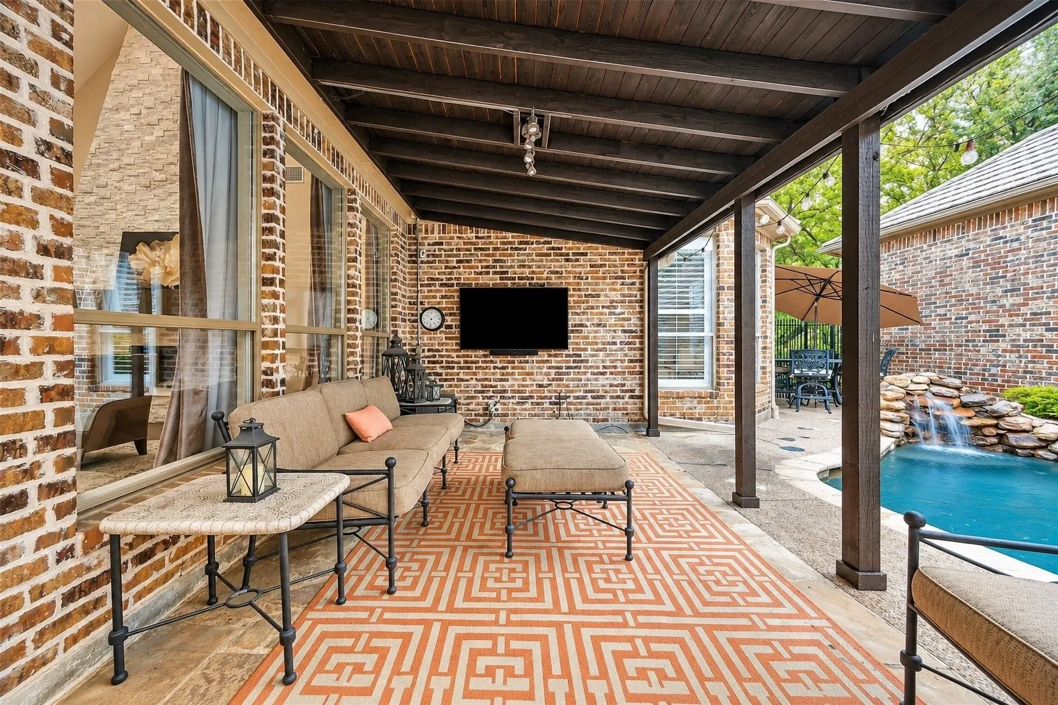 Covered patio with a dark wood-finish ceiling, brick wall, and an integrated television