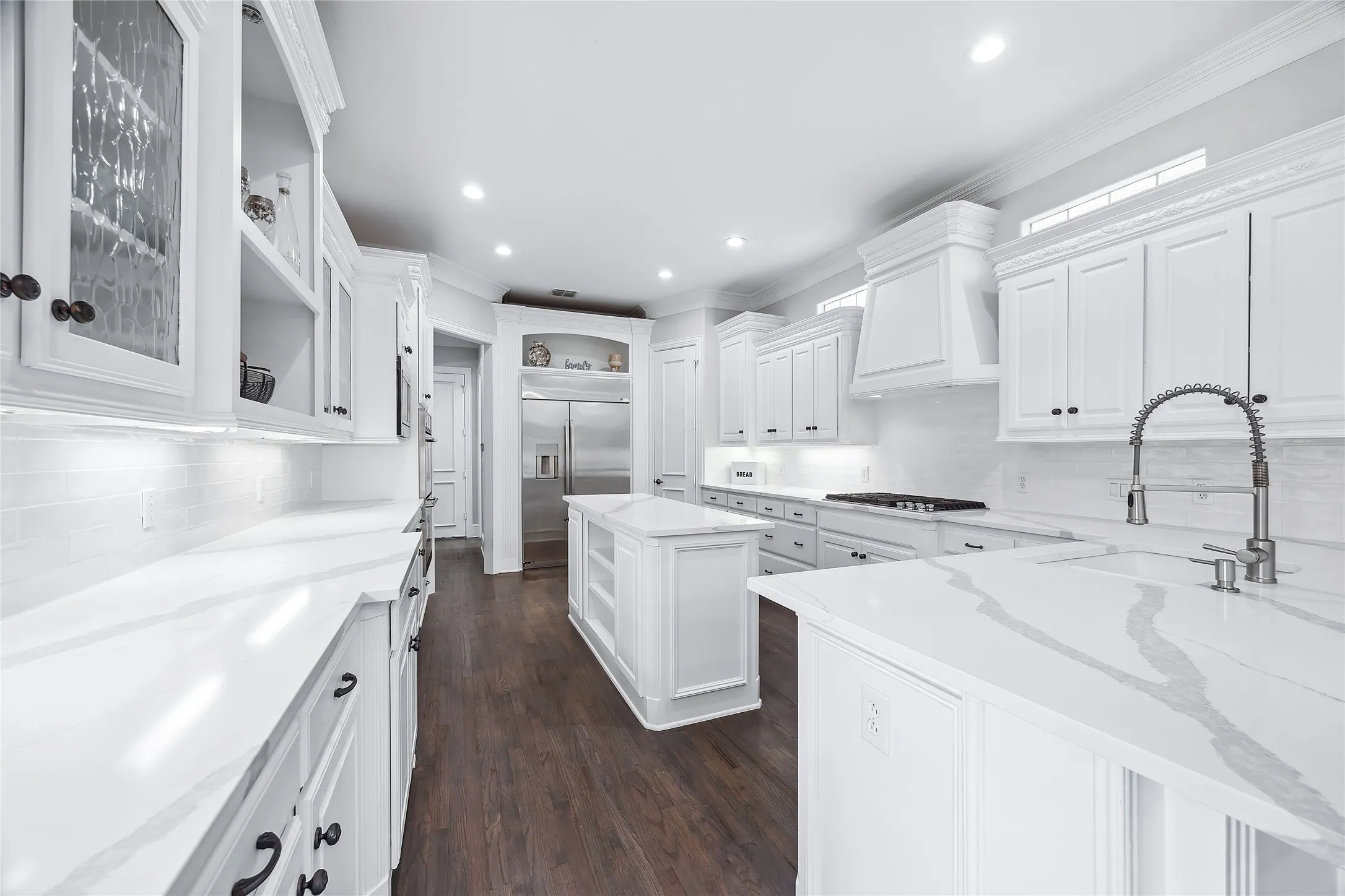 White cabinetry with dark hardware, stone countertops with subtle veining, stainless steel appliances, wood-finish flooring, and recessed lighting