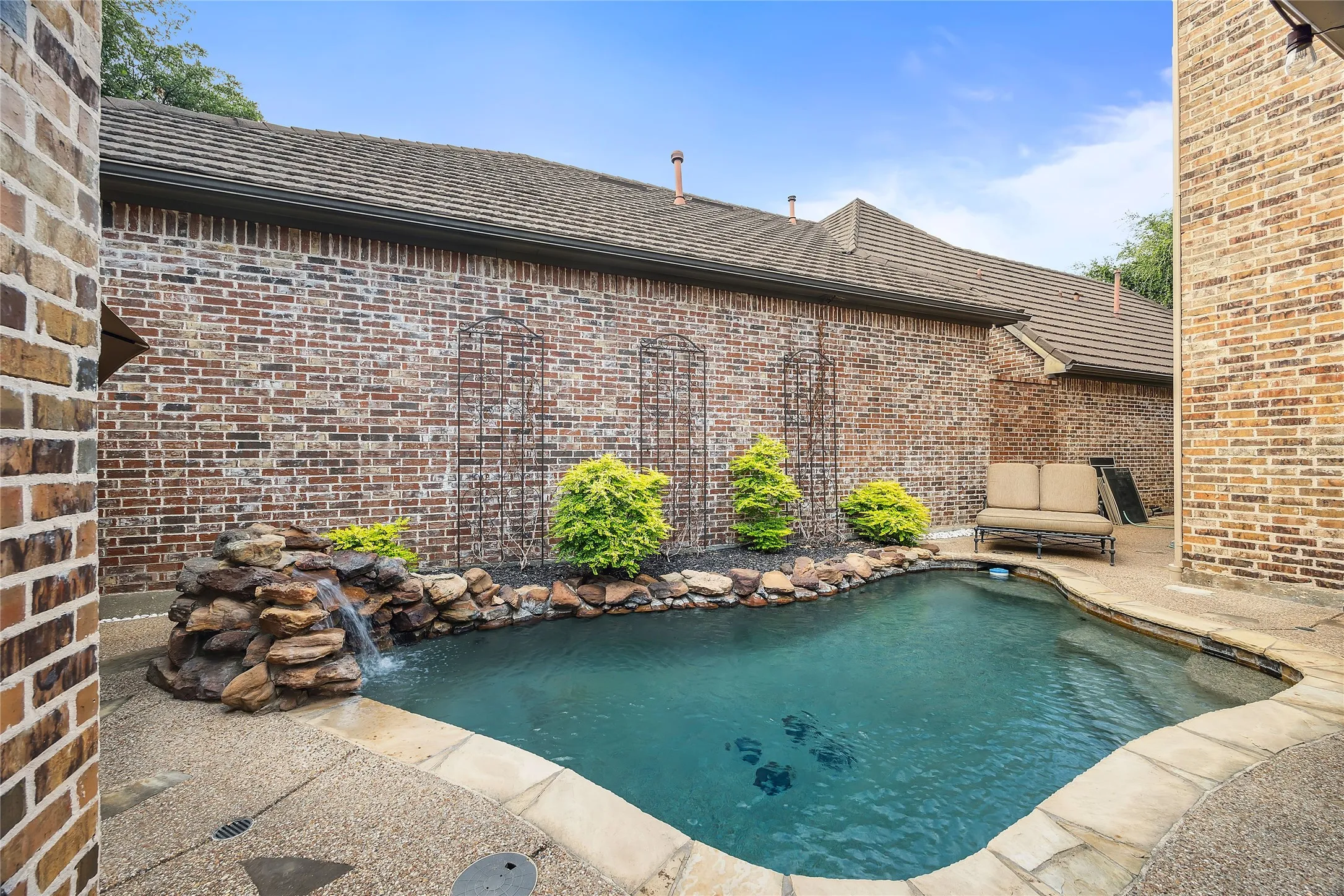 Private swimming pool with stone waterfall feature, surrounded by stamped concrete decking and brick exterior walls