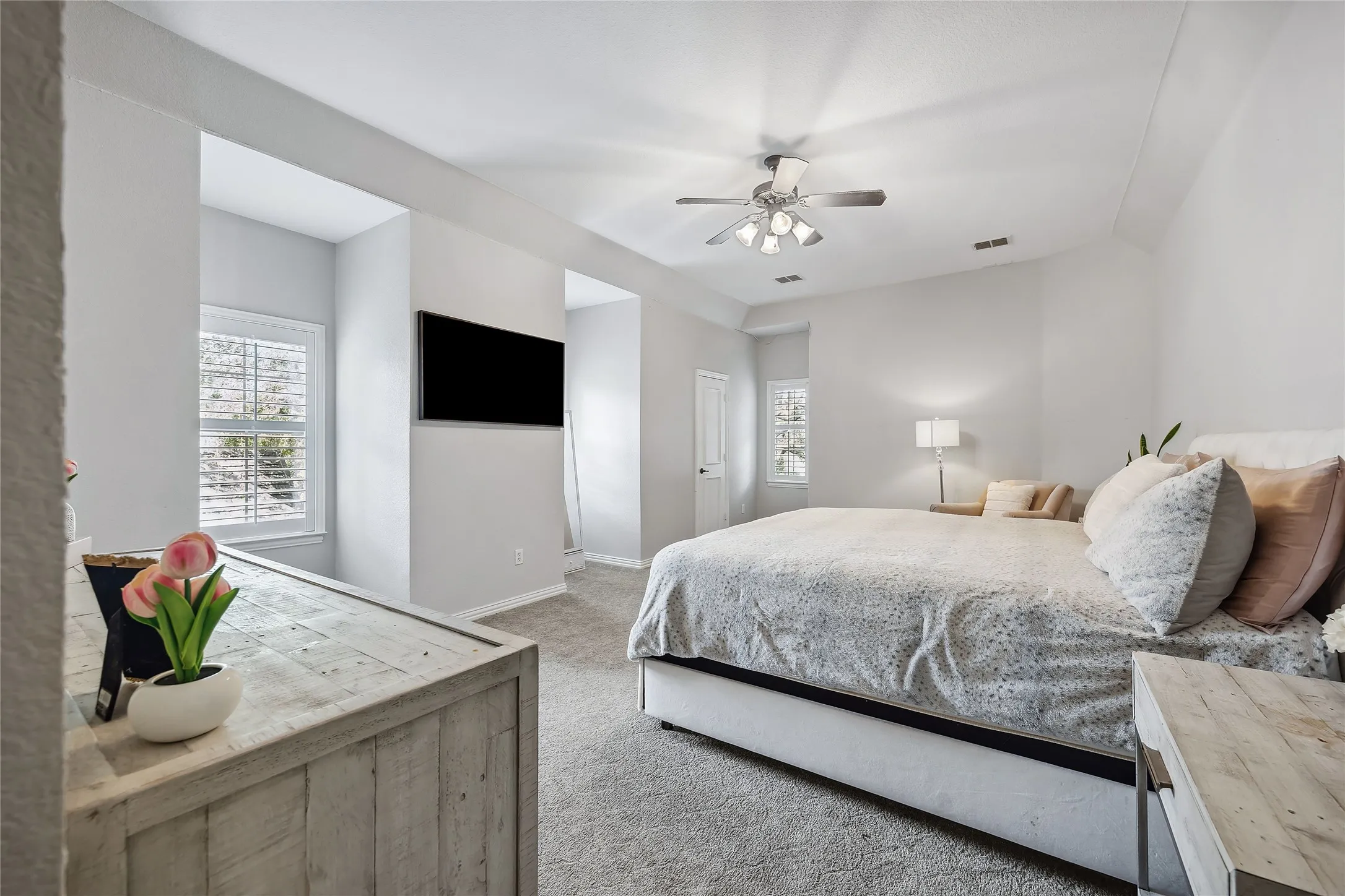Tray ceiling with a ceiling fan, wall-mounted television, and shutters on a window