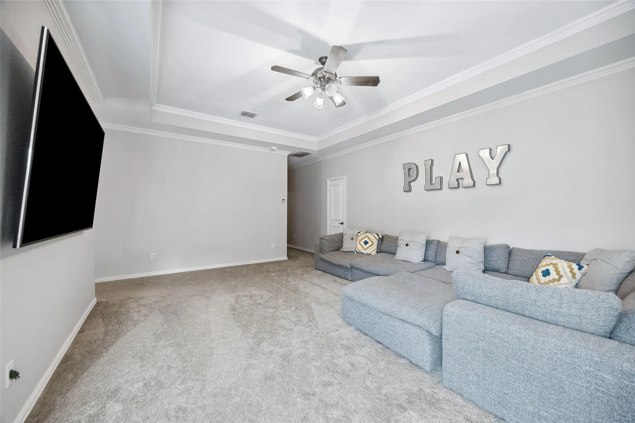 Tray ceiling with crown molding, ceiling fan with integrated lighting, wall-mounted television, and light gray wall paint