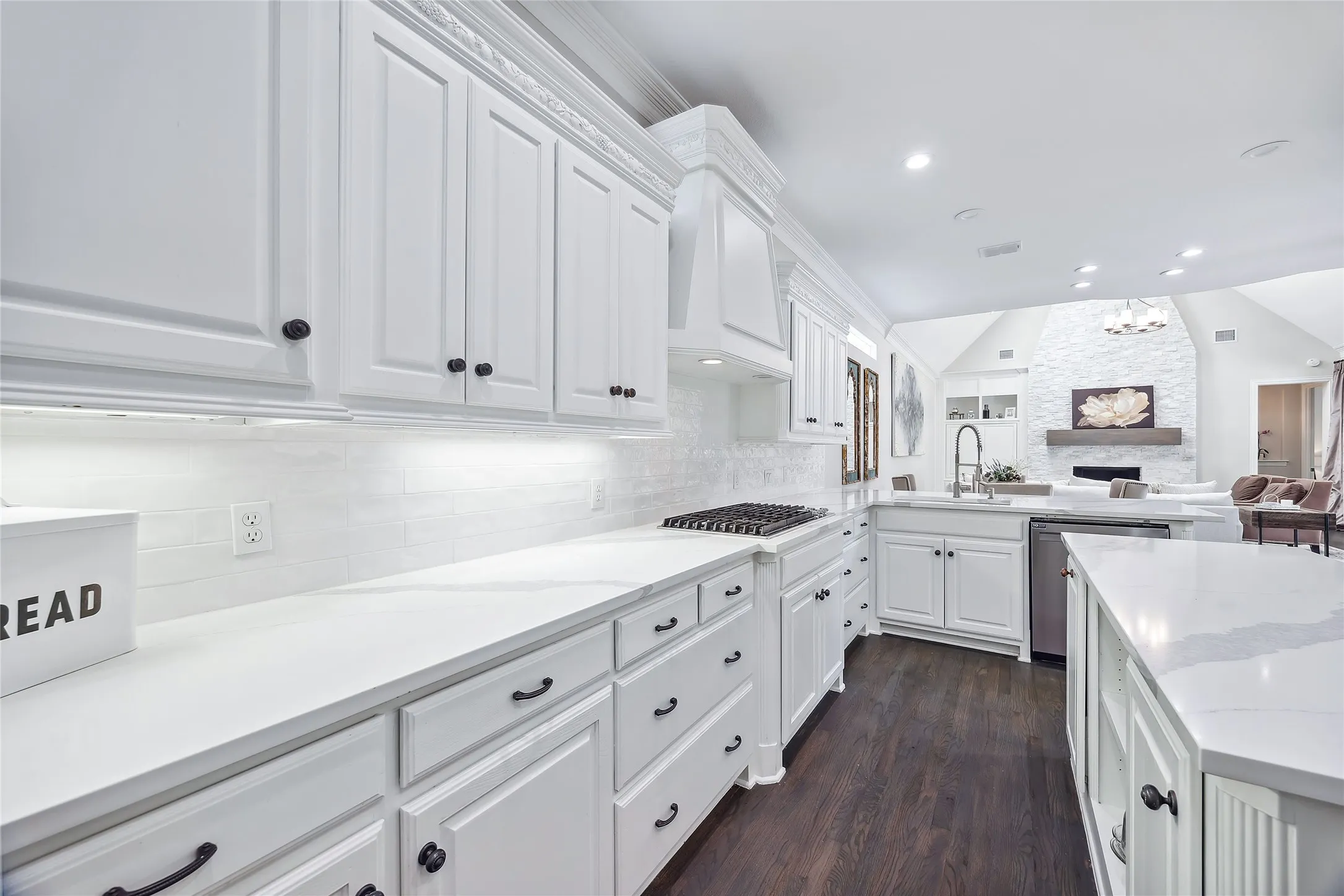 White cabinetry, white countertops, dark wood-finish flooring, white tile backsplash, and a built-in gas range