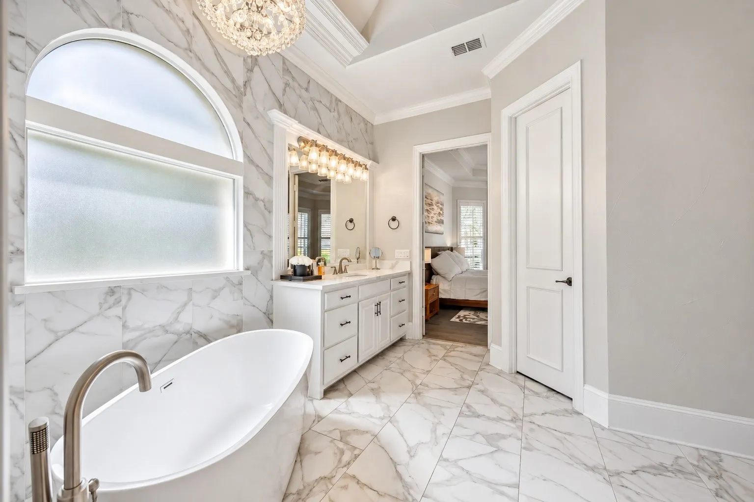 Freestanding soaking tub with brushed nickel fixture, dual vanity with undermount sinks, and marble-look wall and floor tile