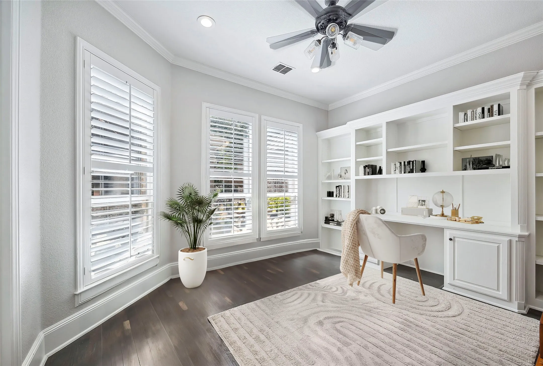 Built-in desk and shelving unit, dark wood-finish flooring, white window shutters, ceiling fan, and recessed lighting