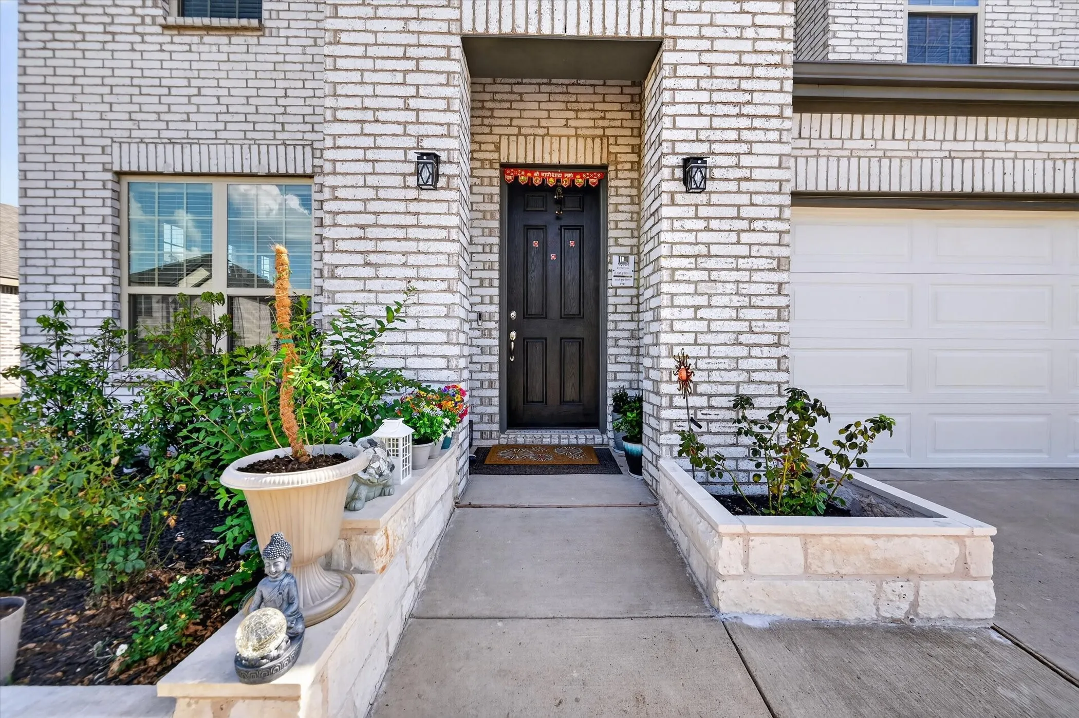 White brick exterior with dark wood entry door, integrated garage, and landscaped planting beds