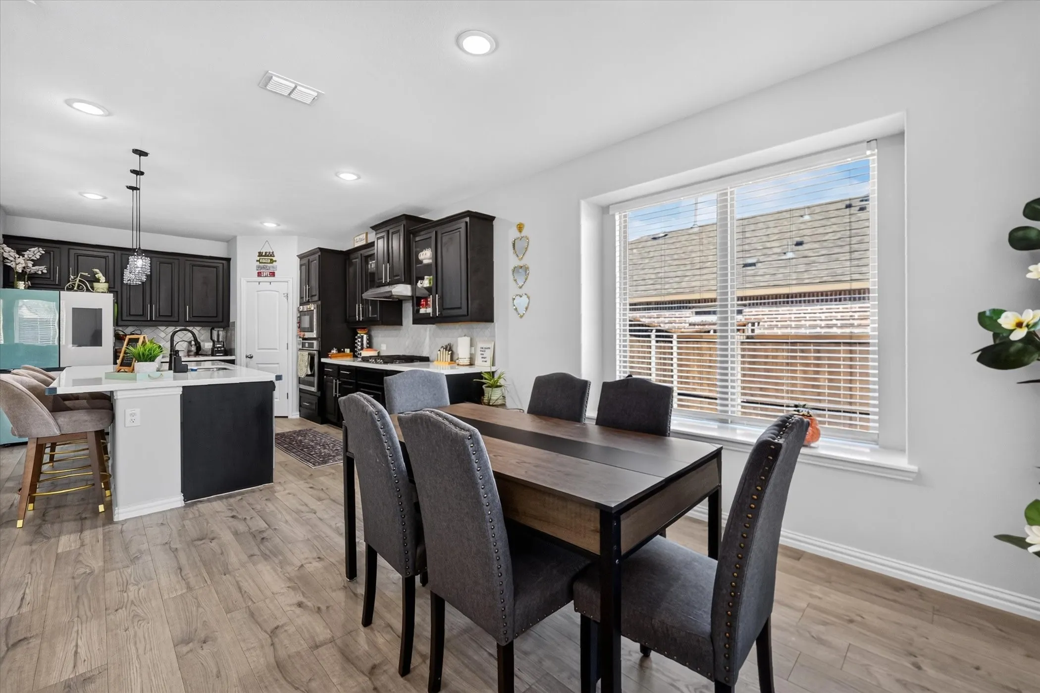 Kitchen and dining area featuring wood-finish flooring, recessed lighting, a kitchen island with seating, dark cabinetry, and a large window