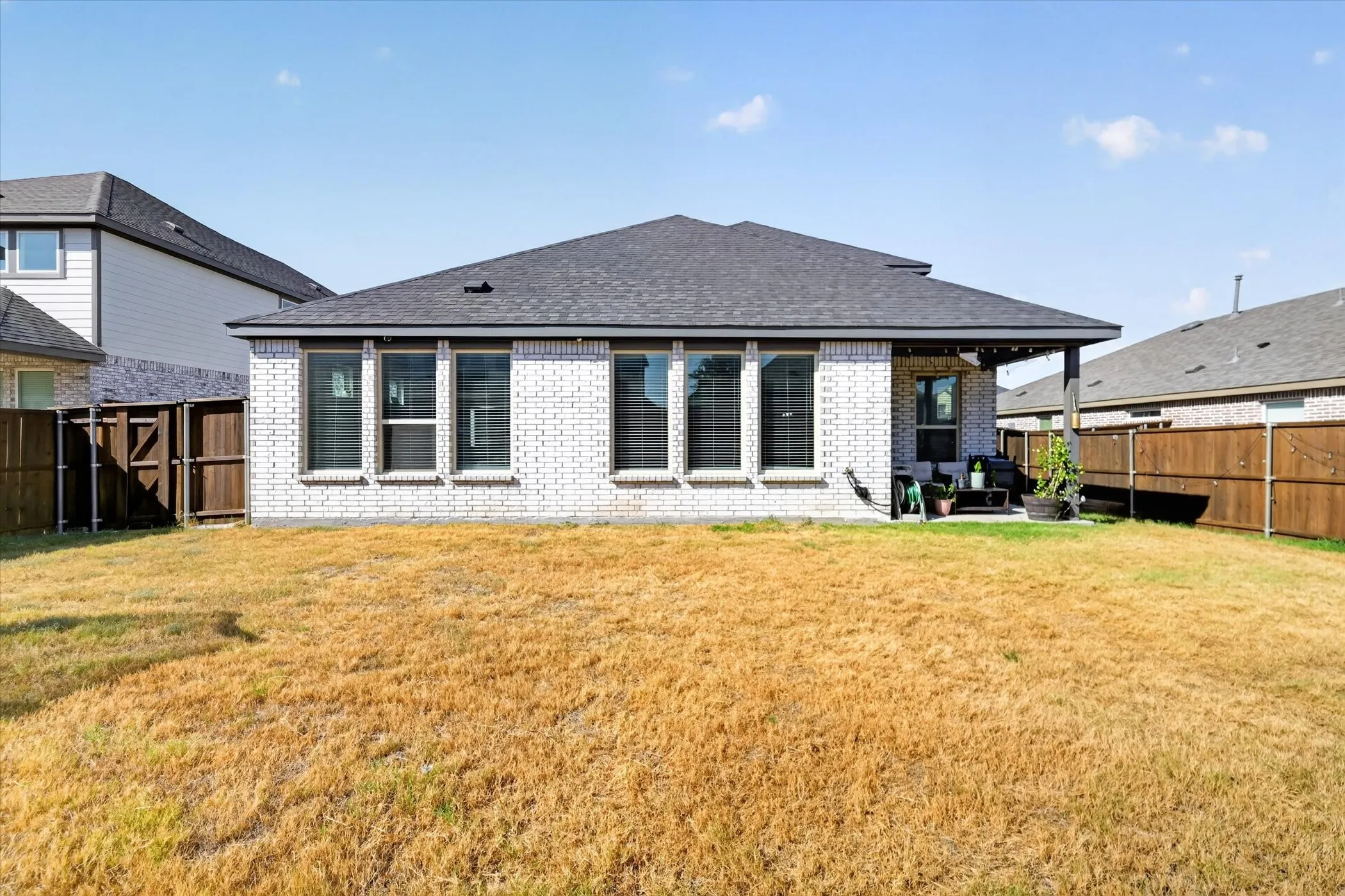 Expansive backyard with a covered patio, privacy fencing, and brick exterior
