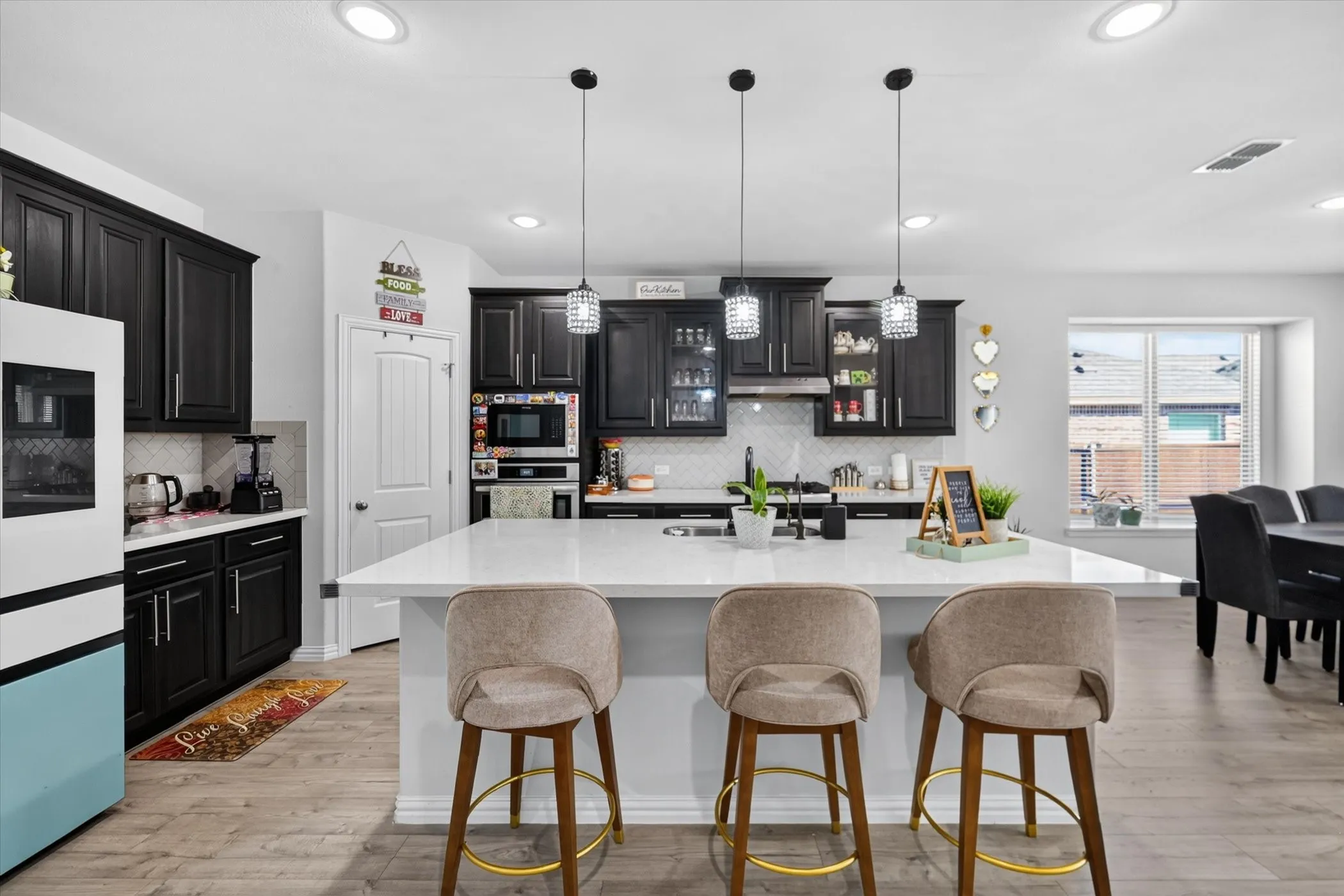 Kitchen featuring dark cabinetry, white countertops, a large island with seating, pendant lighting, and wood-finish flooring