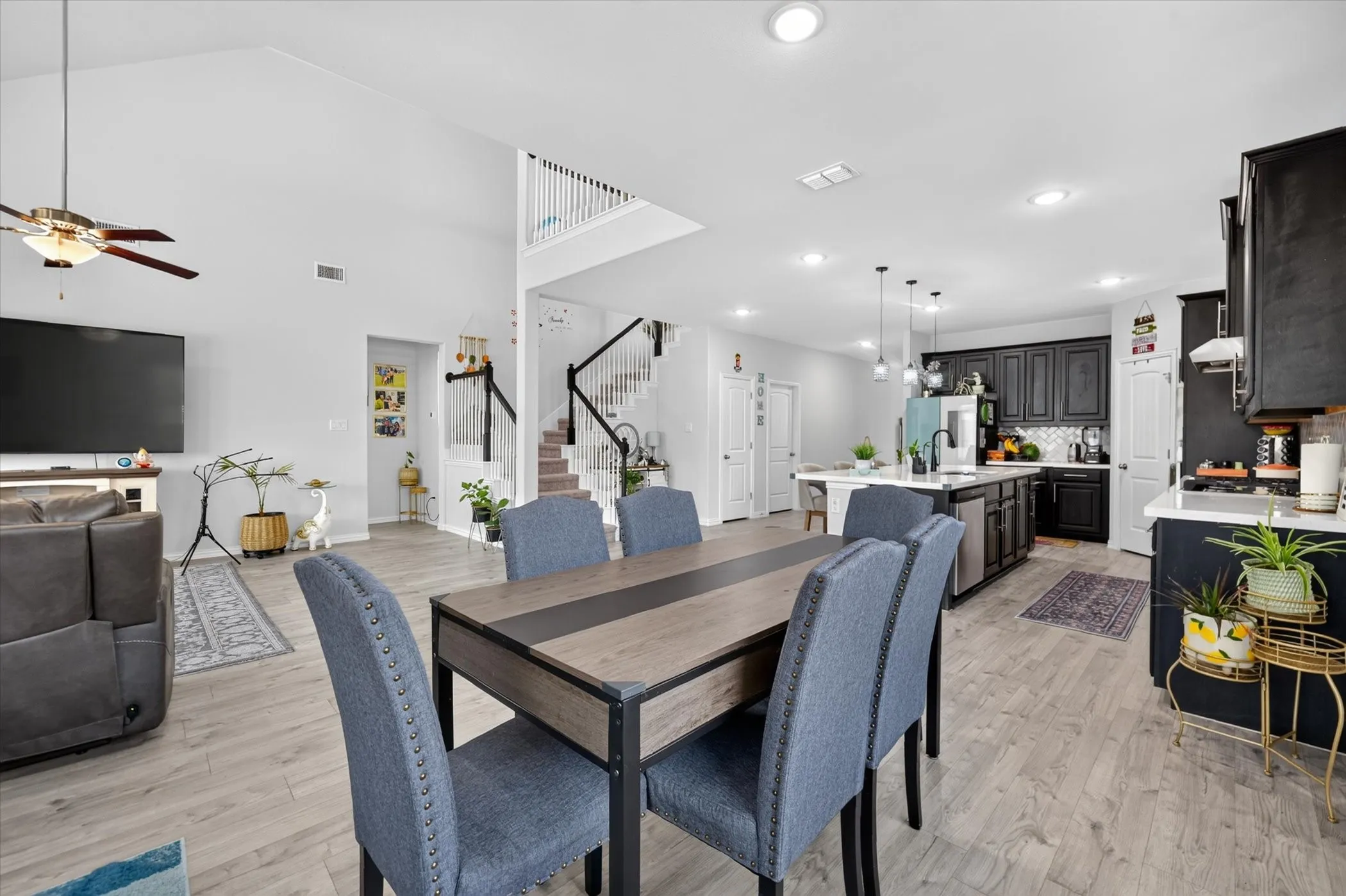 Open-concept living space featuring vaulted ceilings, wood-finish flooring, a modern kitchen with dark cabinetry, and an island with pendant lighting