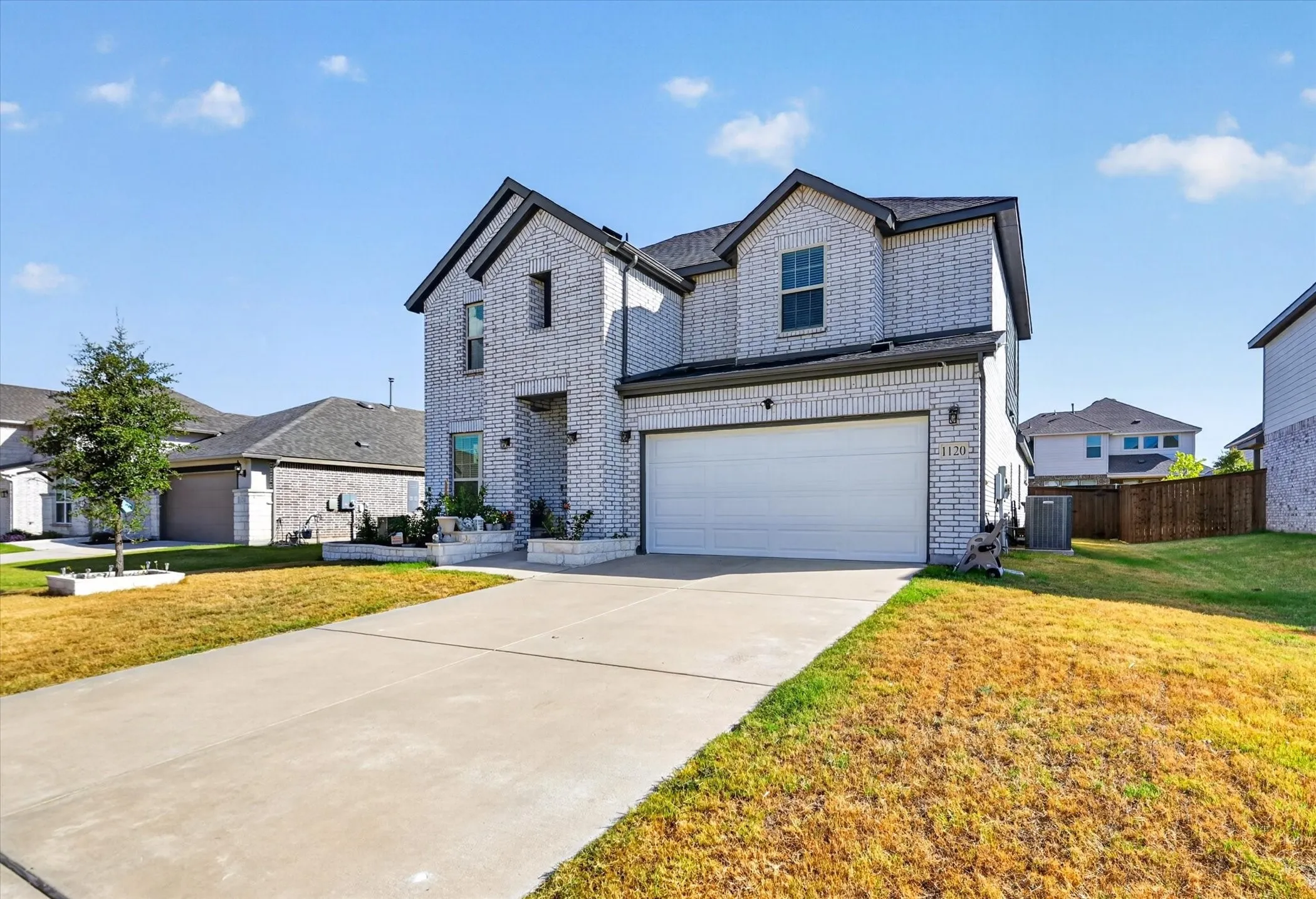 Two-story brick exterior, attached garage, concrete driveway, and established landscaping