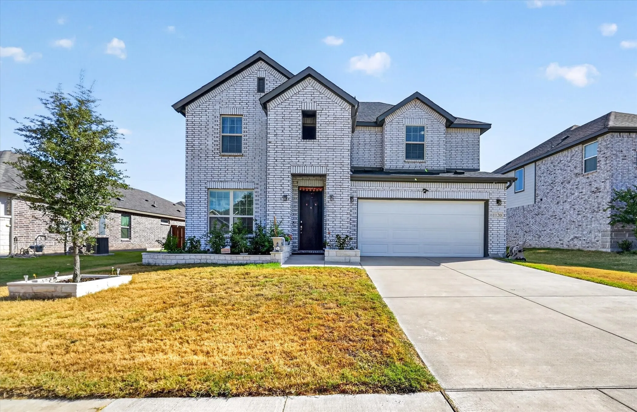 White brick exterior with dark trim accents, attached two-car garage, concrete driveway, and front landscaping