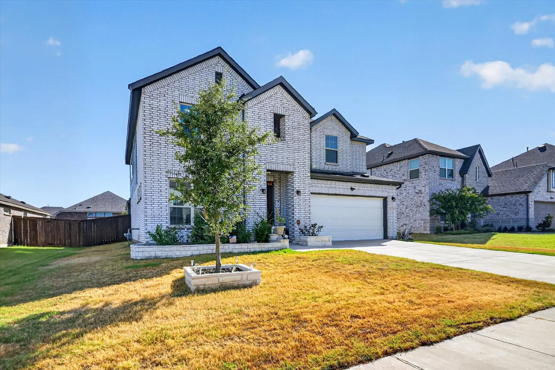 Two-story brick exterior, attached garage, concrete driveway, and a fenced side yard