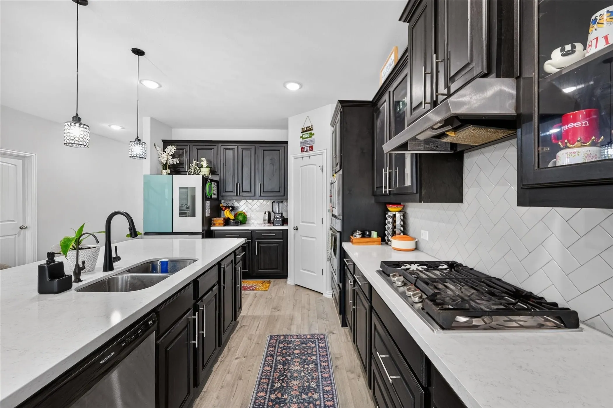 Kitchen featuring dark cabinetry, light countertops, wood-finish flooring, a stainless steel sink with a black faucet, and pendant lighting