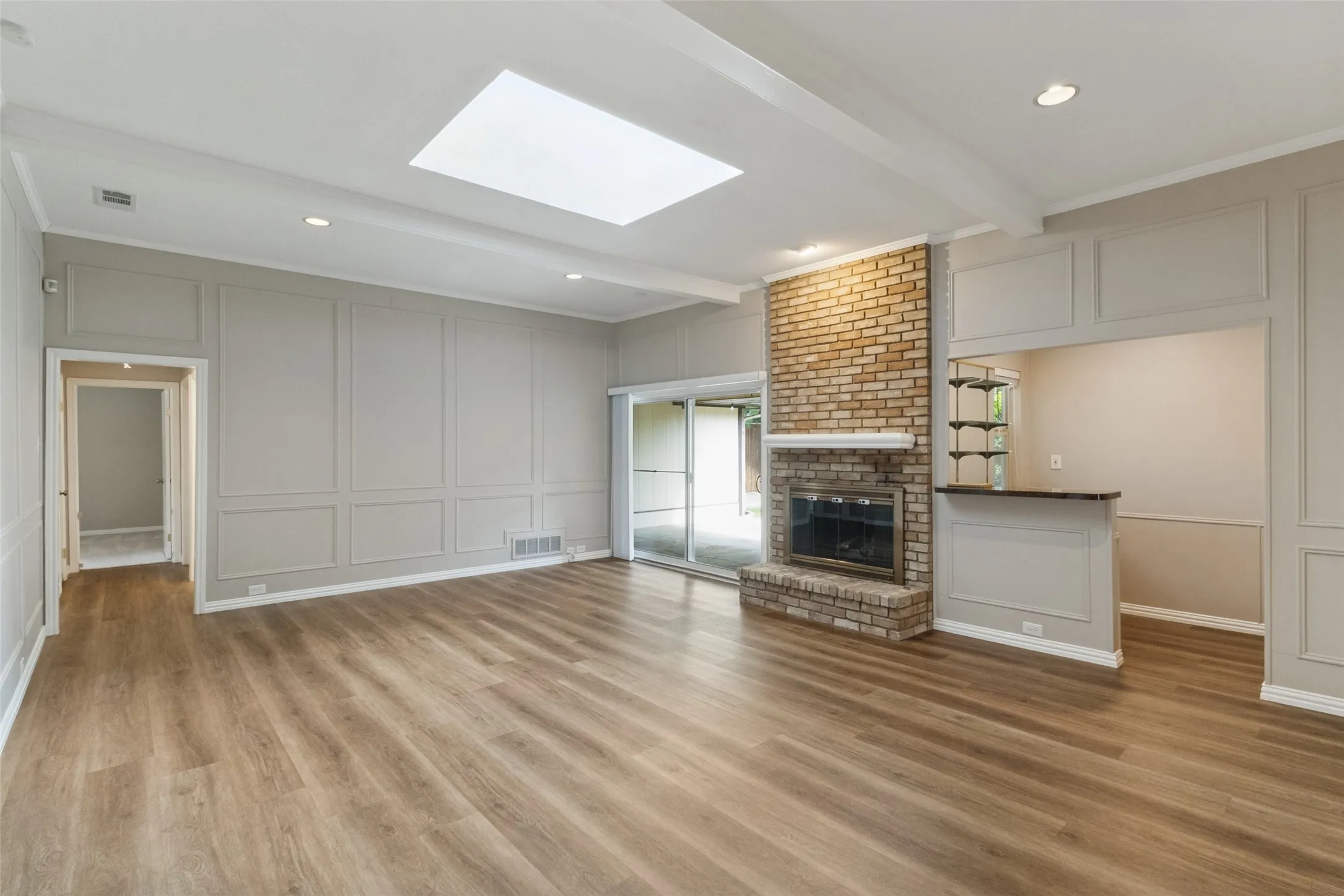 Wood-finish flooring throughout, brick fireplace, built-in wet bar, skylight, and sliding glass doors