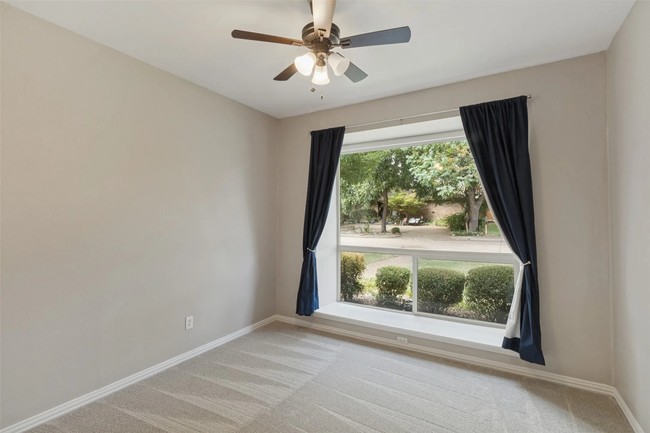 Wall-to-wall carpeting, bay window with integrated sill, ceiling fan with light fixture, and light-toned wall paint