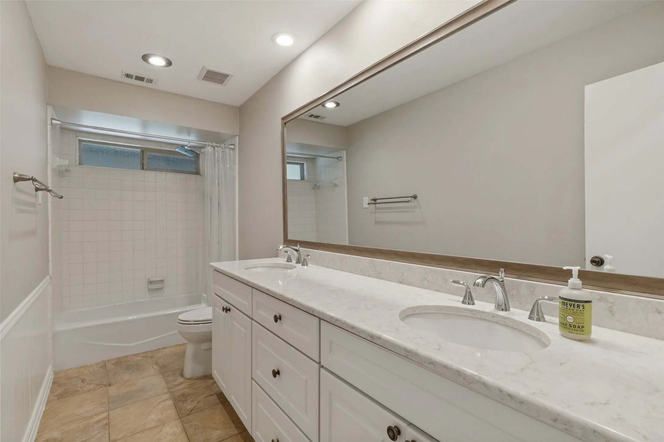 Dual vanity with undermount sinks, stone countertop, white cabinetry, and a full-width mirror