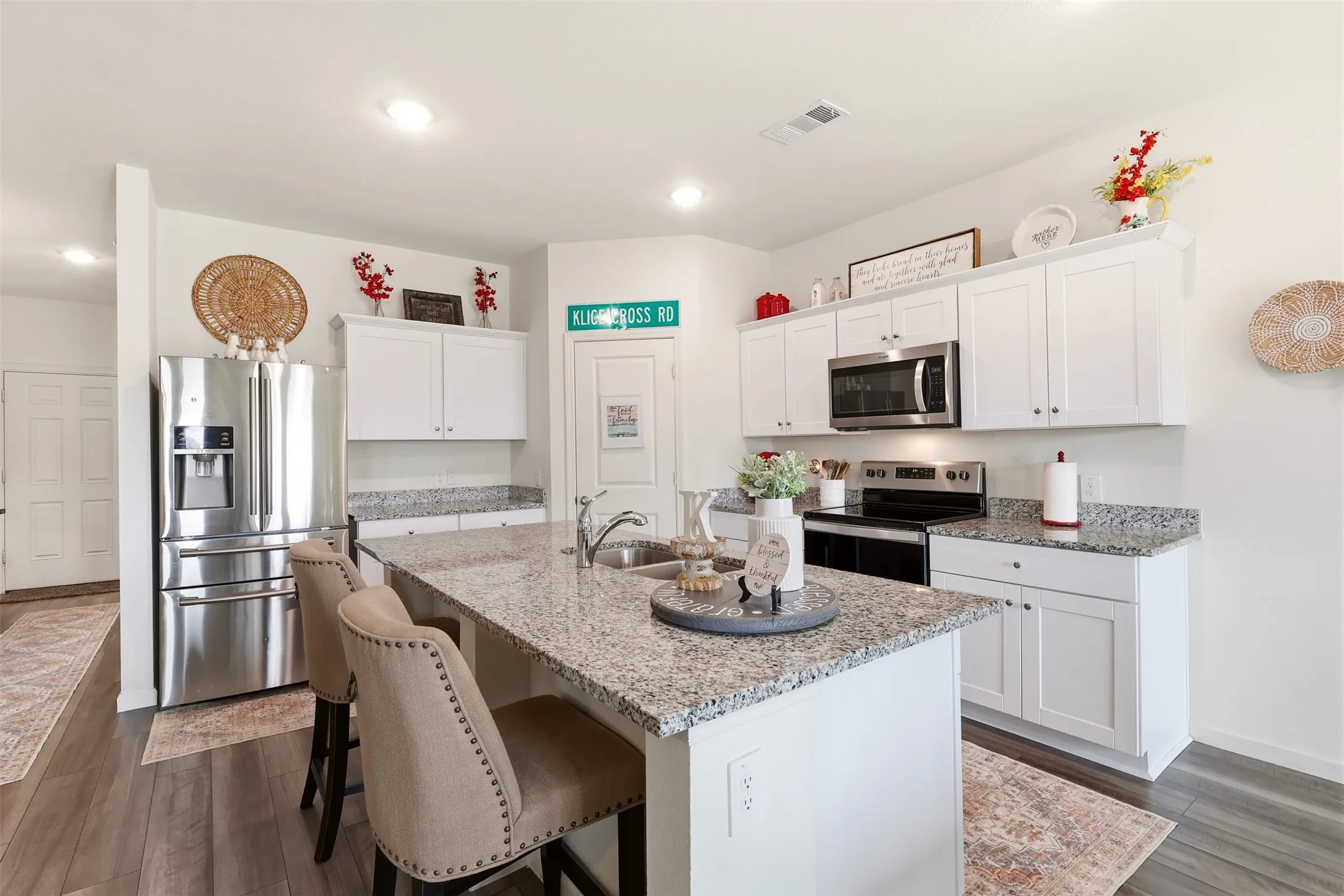 Contemporary kitchen featuring white cabinetry, stainless steel appliances including a French-door refrigerator and built-in microwave, granite-style countertops, and a large center island with seating