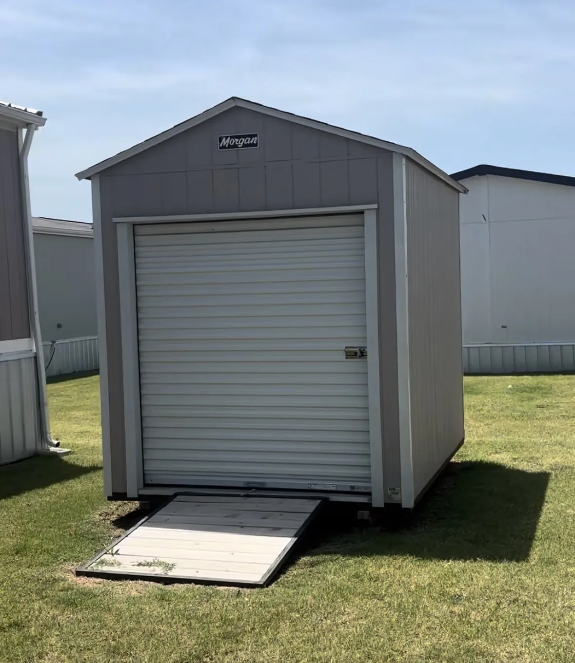 Storage shed with a roll-up door, wood-paneled siding, and a sloped ramp included