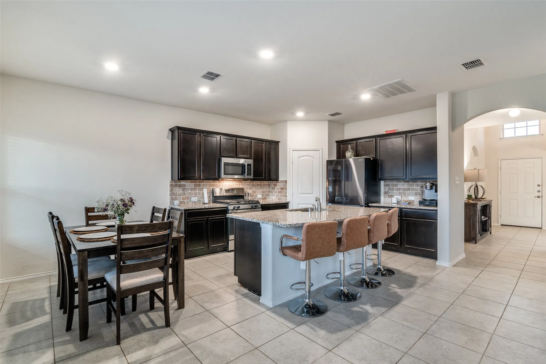 Kitchen featuring dark wood cabinetry, stainless steel appliances, a tile backsplash, and a granite island with seating