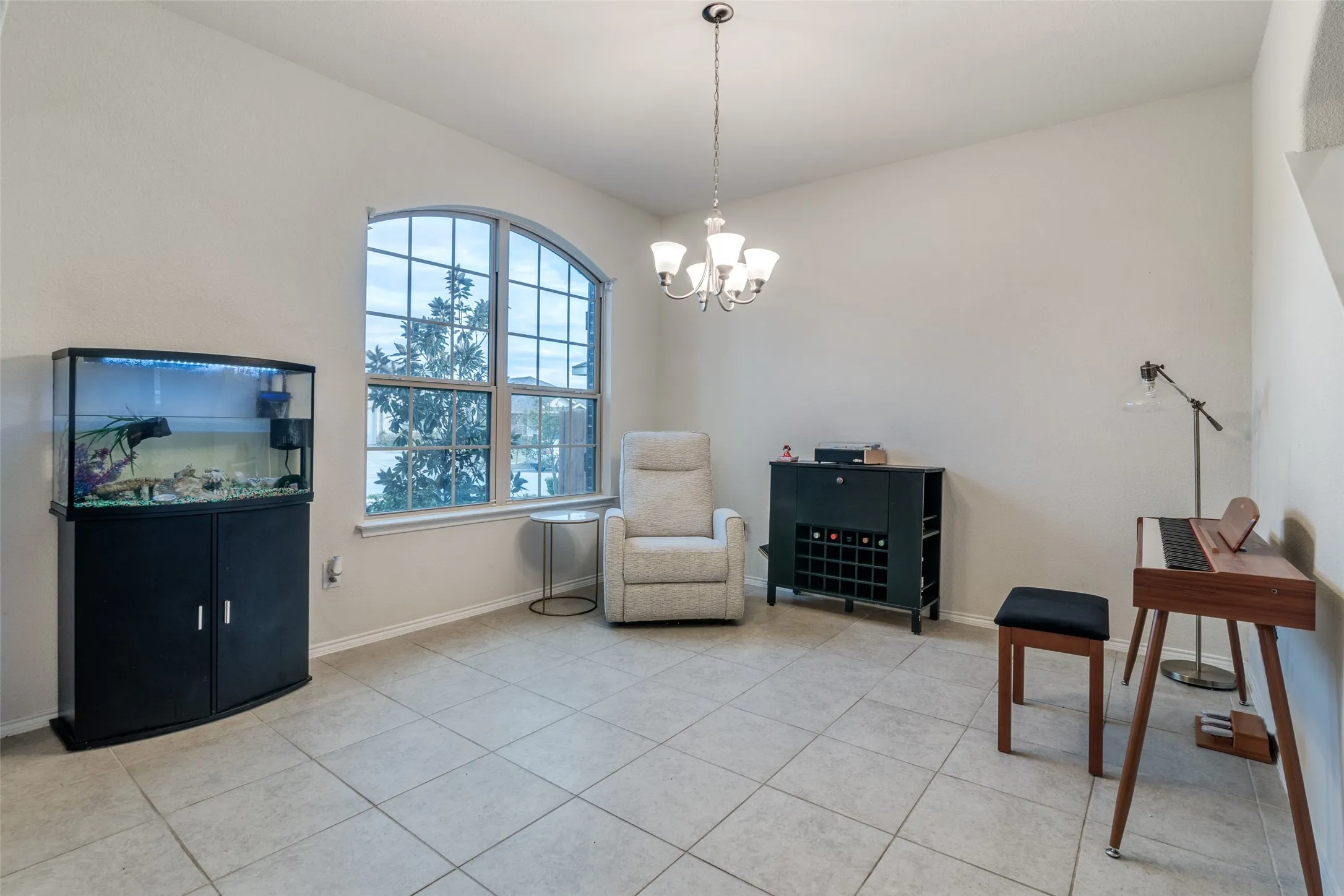 Arch-top window with grid pattern, neutral tile flooring, and a multi-light chandelier