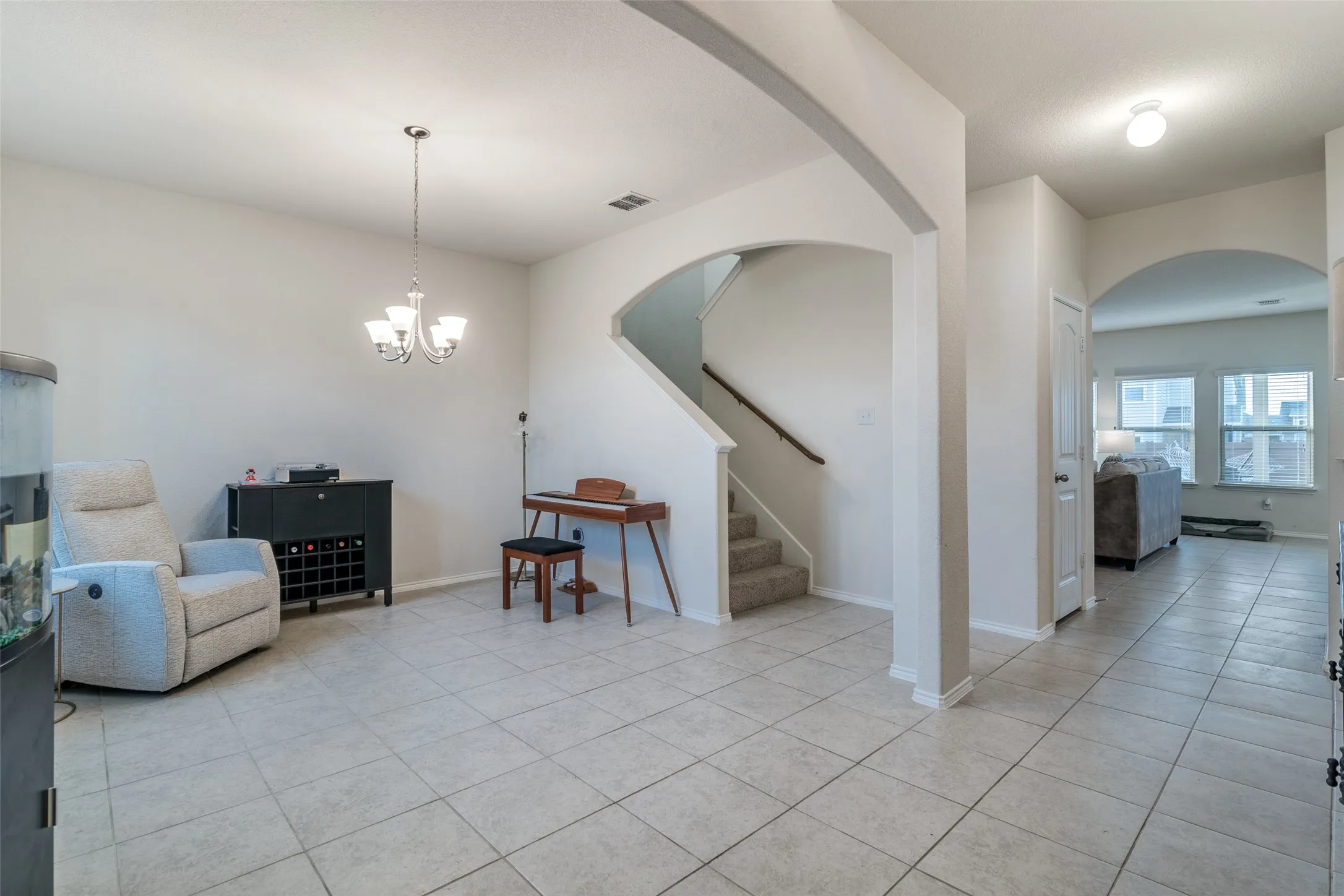 Tiled flooring throughout, chandelier light fixture, arched doorways, and carpeted stairs with a handrail