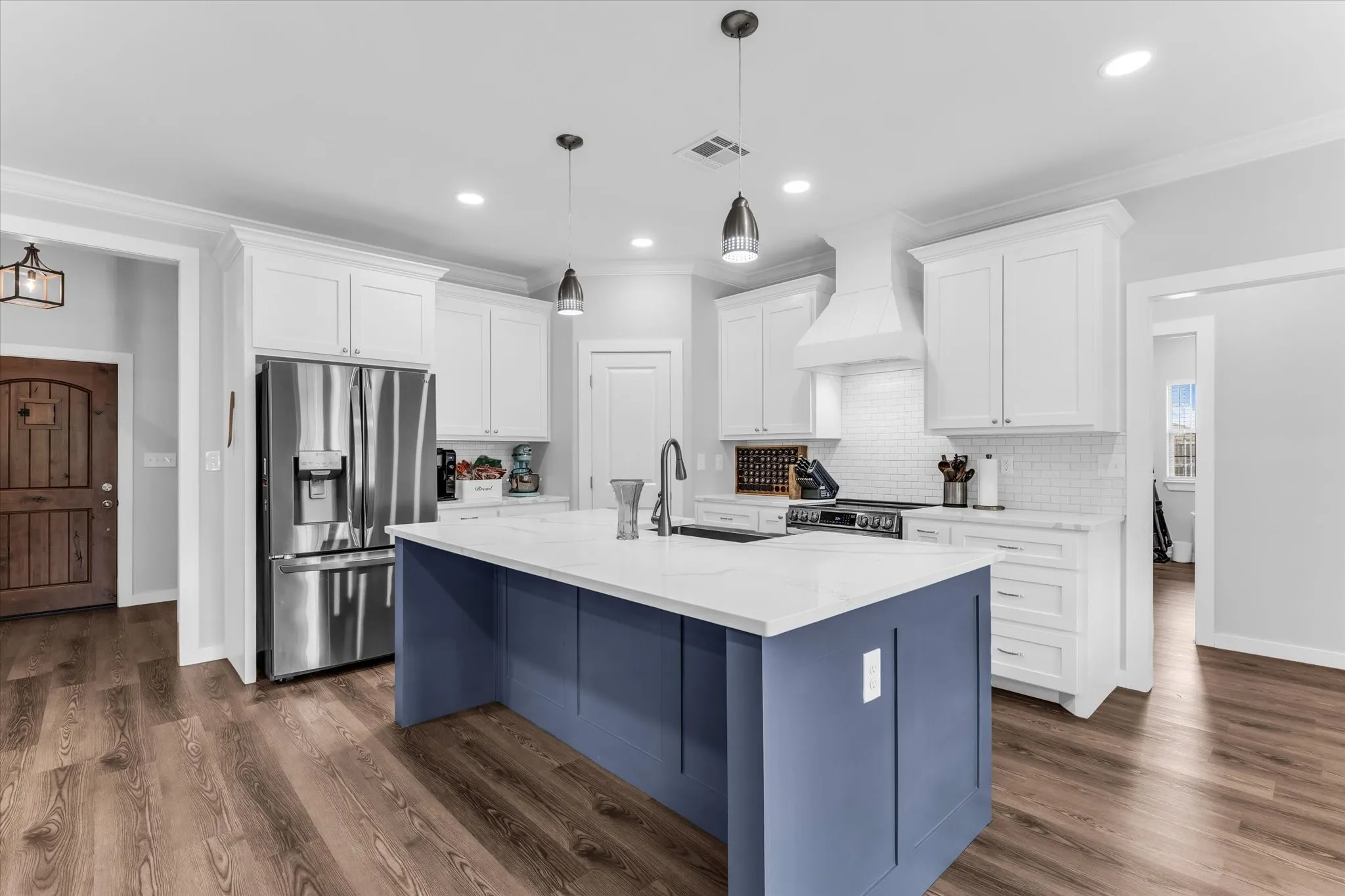 Kitchen featuring a blue island with a white countertop, stainless steel appliances, white cabinetry, subway tile backsplash, and wood-finish flooring