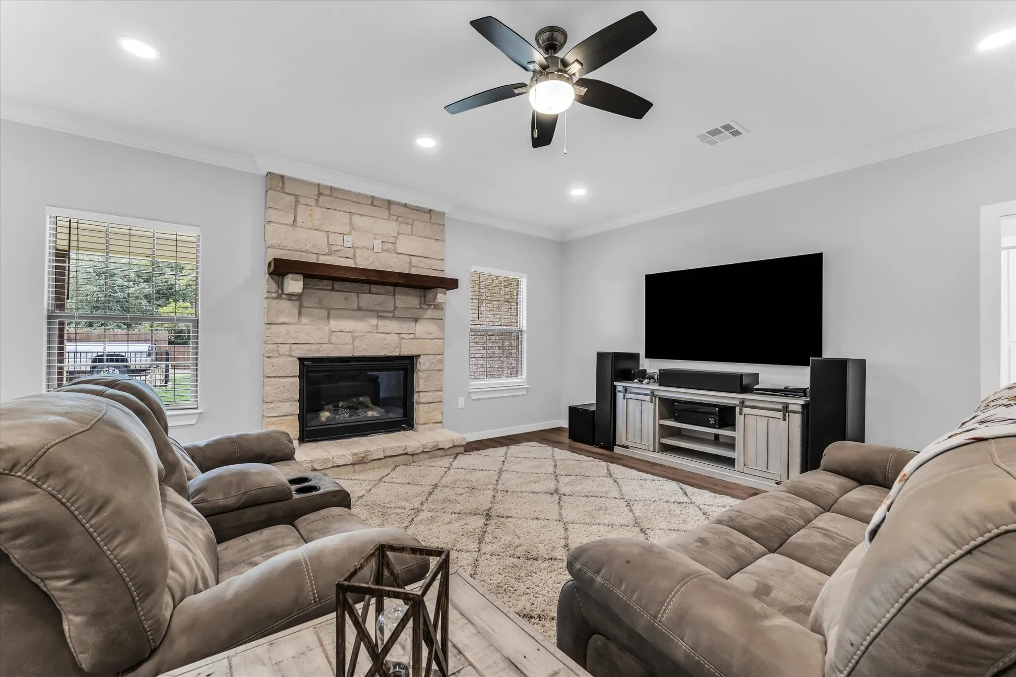 Stone-surround fireplace with a wood mantle, wood-finish flooring, and recessed lighting