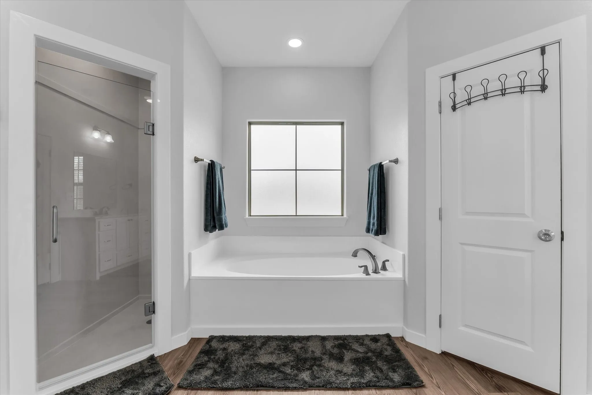 Built-in soaking tub with dark-finish fixtures, a frosted window, and wood-finish flooring