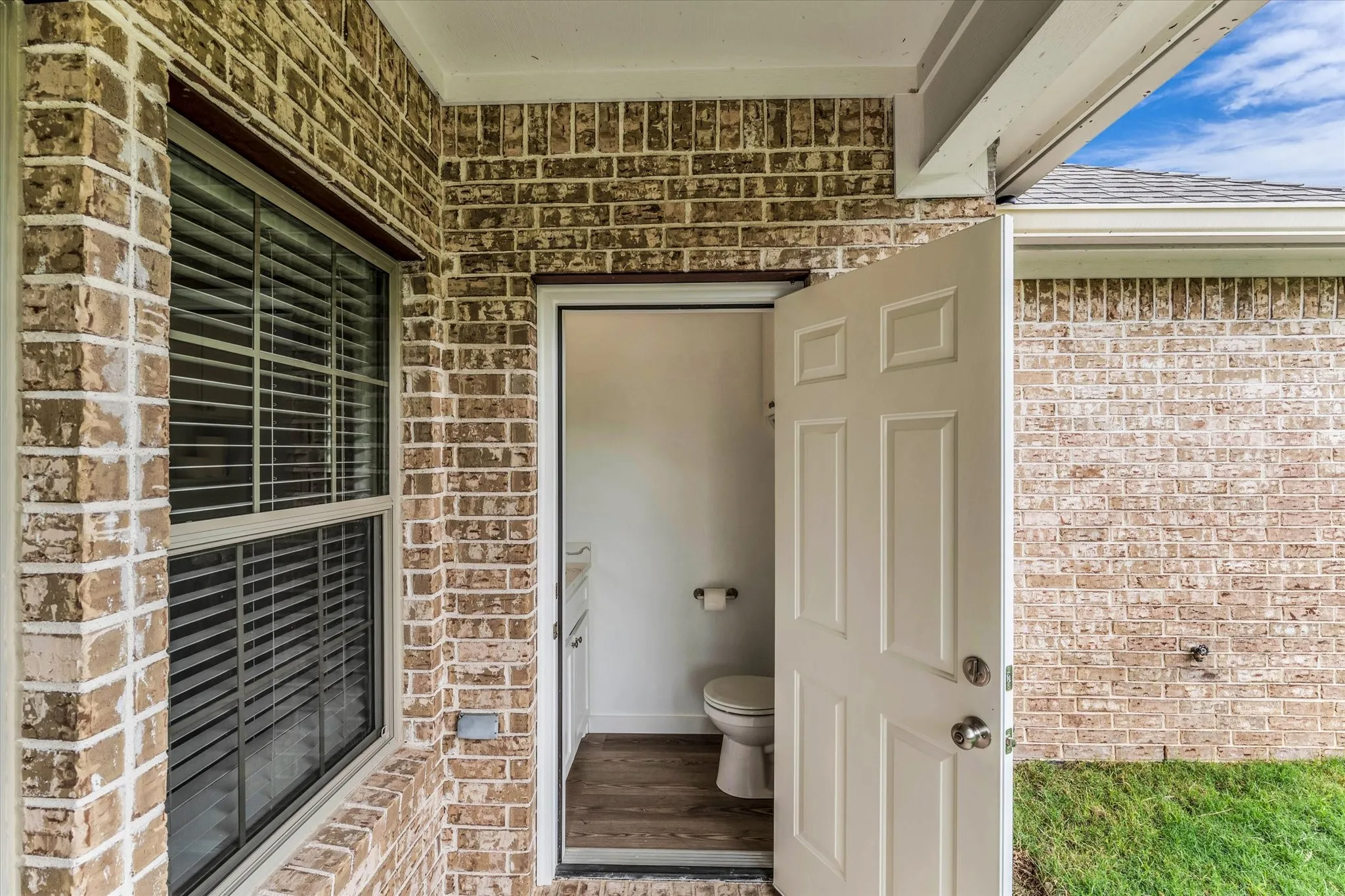 Brick exterior with a covered entryway, a white panel door, and a ground-level window