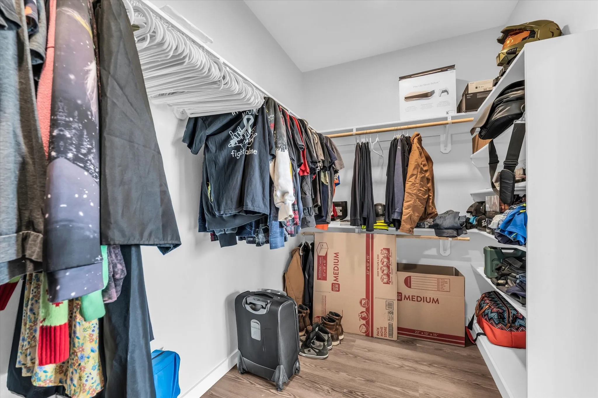 Walk-in closet with multiple hanging rods, wood-finish flooring, and built-in shelving