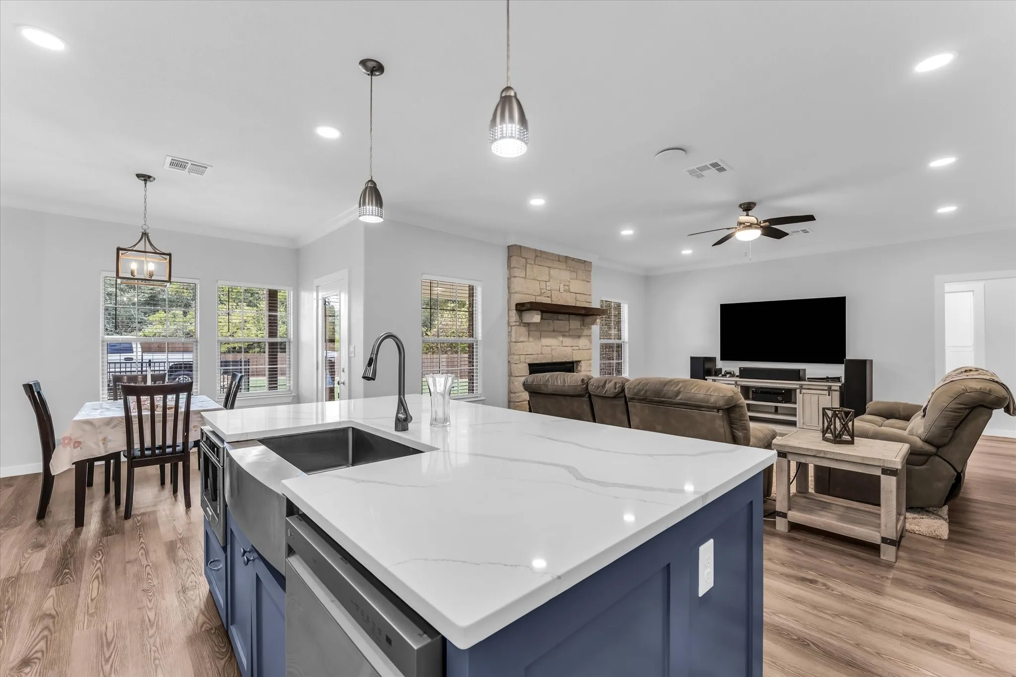 Spacious open-concept interior featuring wood-finish flooring, a kitchen island with a farmhouse sink and quartz countertop, and a living area with a stone fireplace