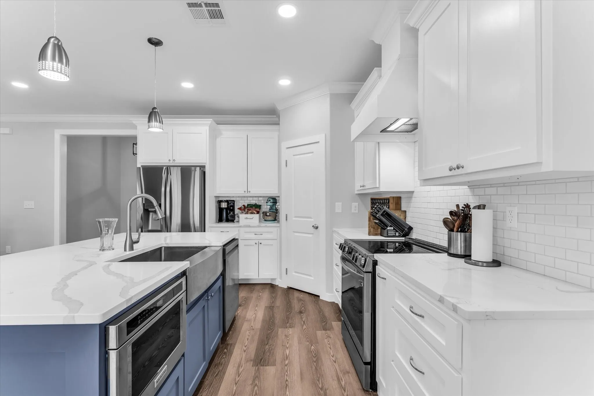 Kitchen featuring white shaker cabinetry, stainless steel appliances, wood-finish flooring, white subway tile backsplash, and an island with a farm sink