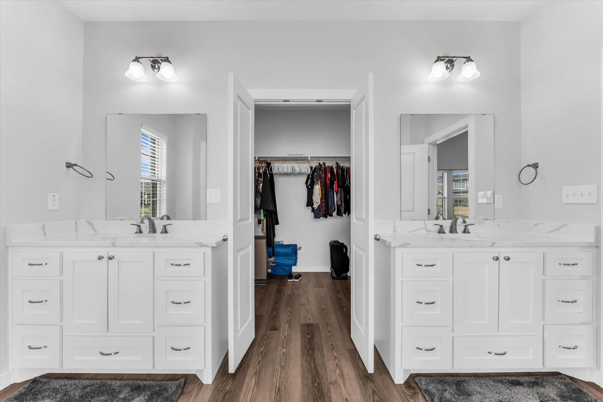 Dual white vanity cabinets with integrated sinks, individual mirrors, and wall-mounted light fixtures